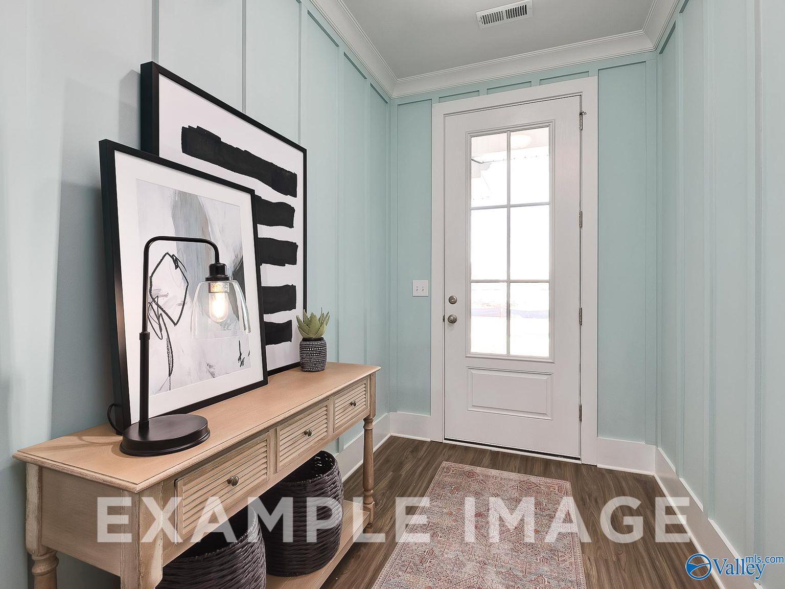 Elegant entryway featuring light blue walls, wooden console table with lamp and abstract art, glass door in Davidson Homes The Everett B, Toney, Alabama