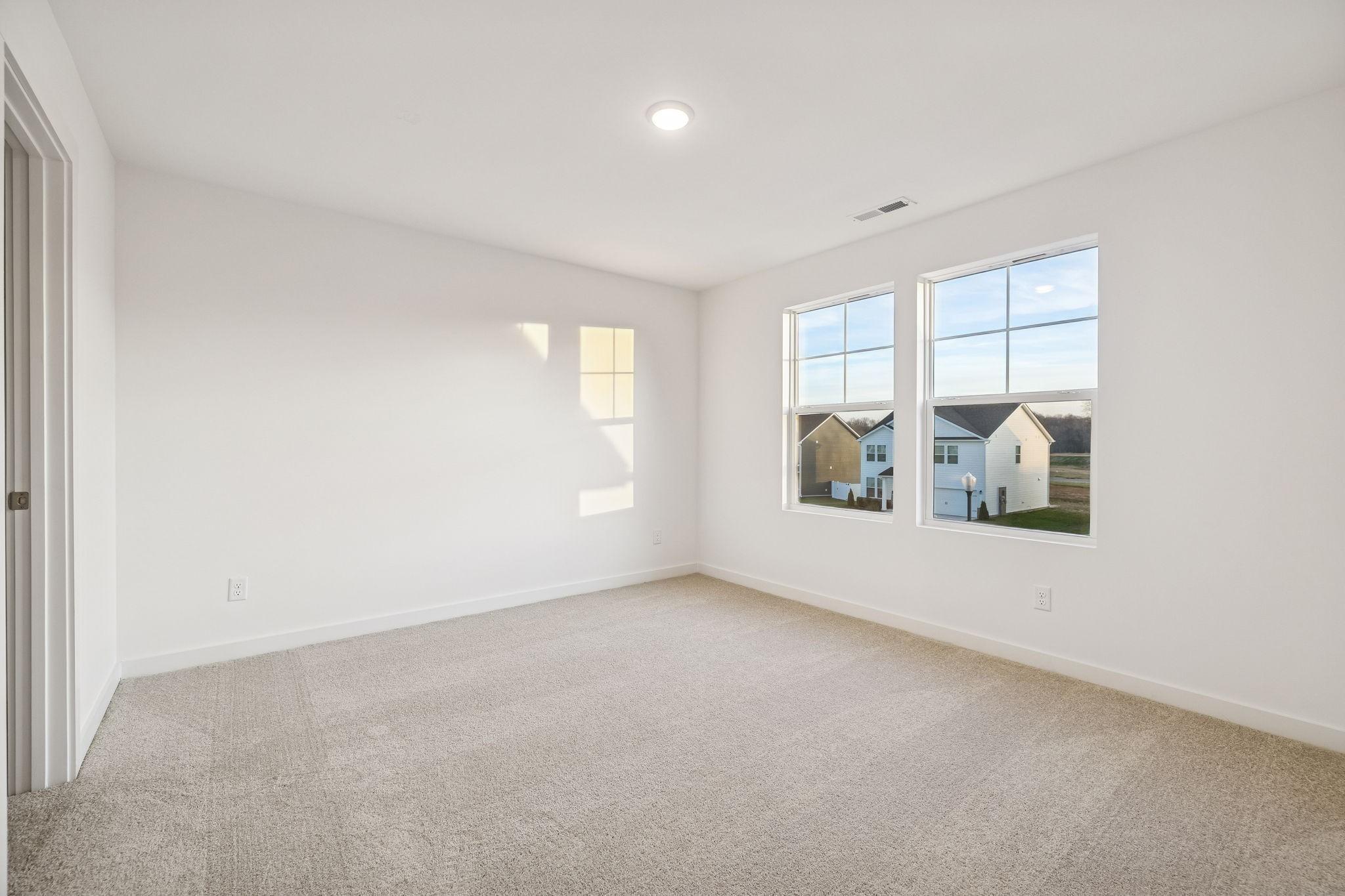 Bright bedroom featuring white walls, beige carpet, and large window overlooking neighborhood homes in Davidson Homes The Willow, Calista Farms, White House, TN