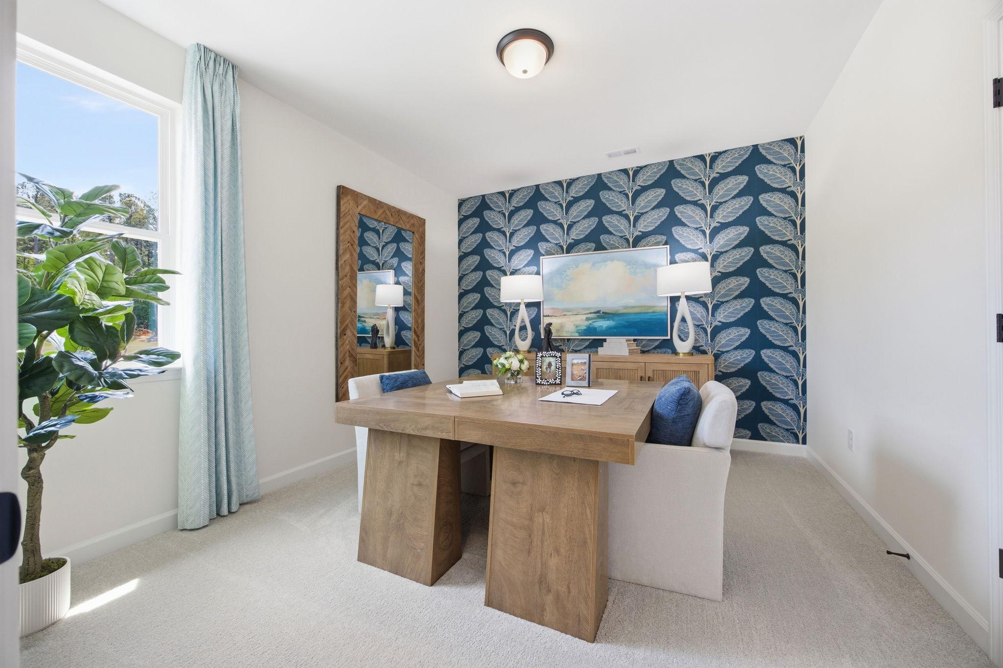 Stylish home office at Sage on North Main in Wake Forest NC featuring wooden desk, navy leaf wallpaper, and fiddle leaf plant
