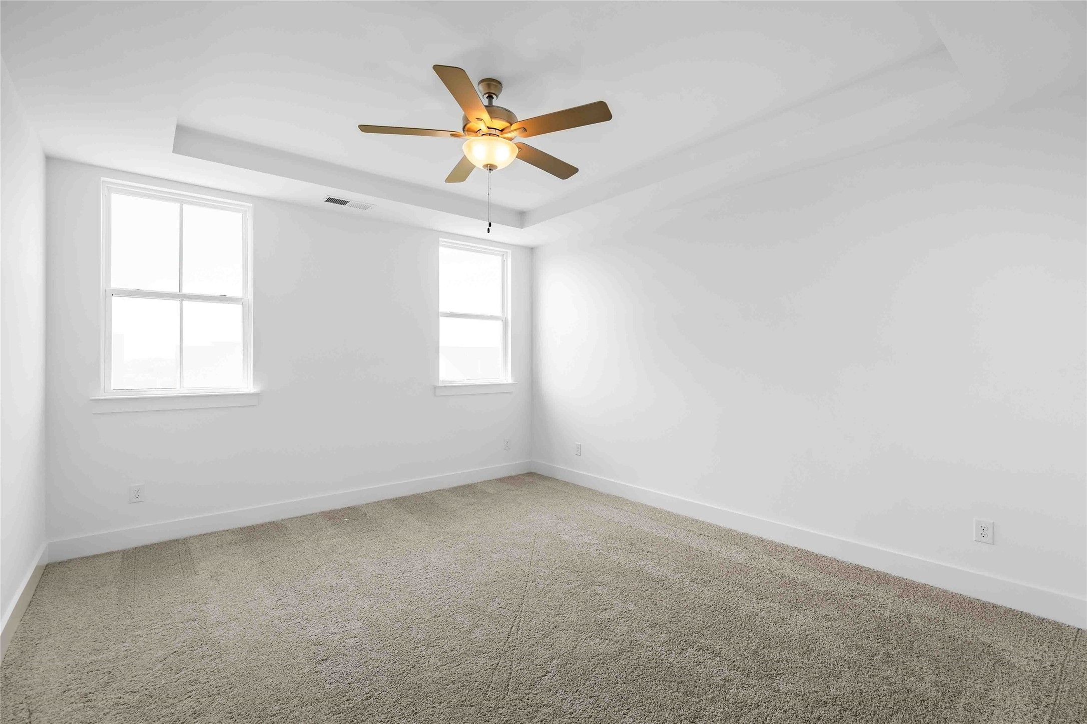Bright bedroom with tray ceiling and ceiling fan in The Ash O floor plan by Davidson Homes in Heartland, Texas.