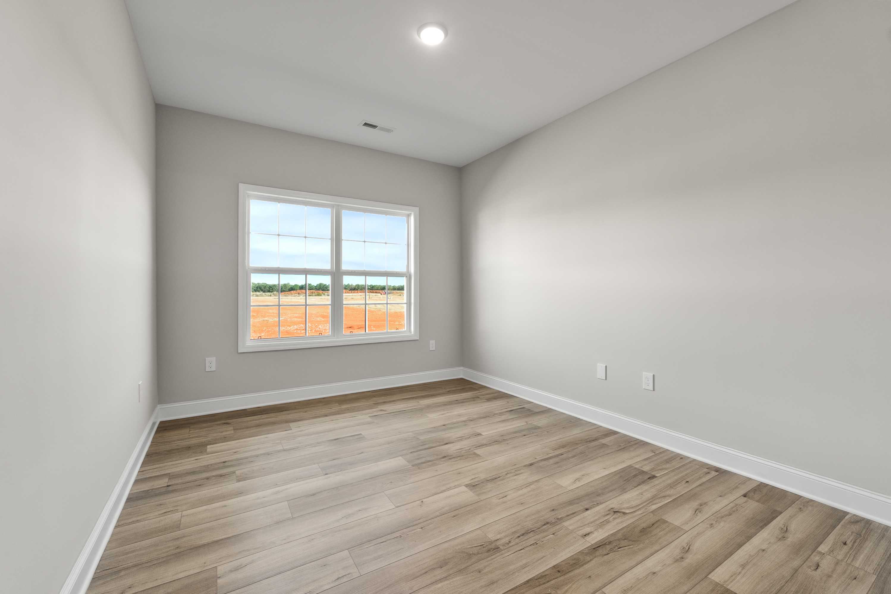 Spacious bedroom in The Valencia home design with light gray walls, hardwood floors, and large window overlooking scenic view