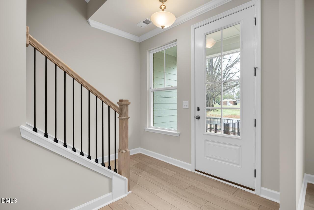 Elegant foyer with oak staircase, black iron balusters, hardwood floors, white glass door, and window overlooking lawn in Davidson Homes The Avery, Knightdale NC