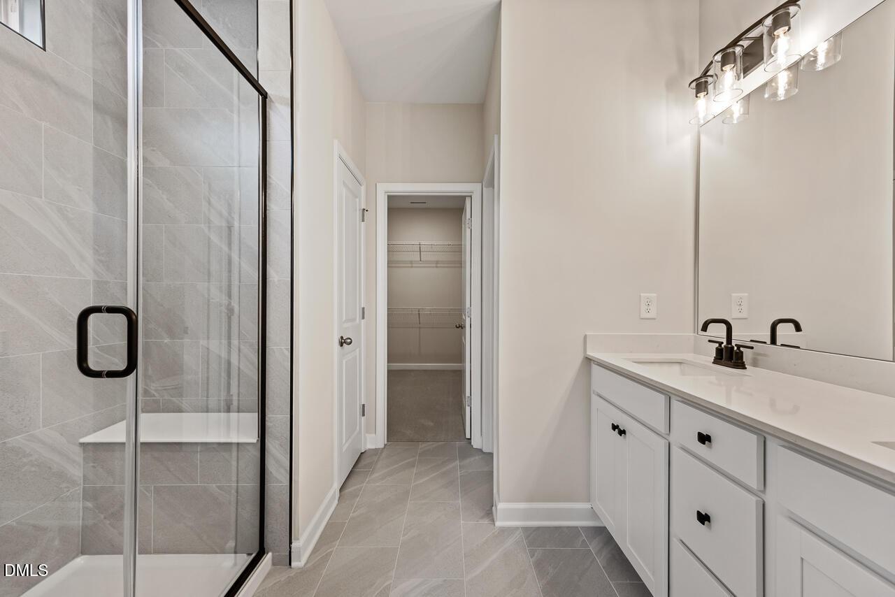 Modern master bathroom with glass-enclosed shower, dual vanity, and walk-in closet in The Ash C floor plan, Zebulon, NC.