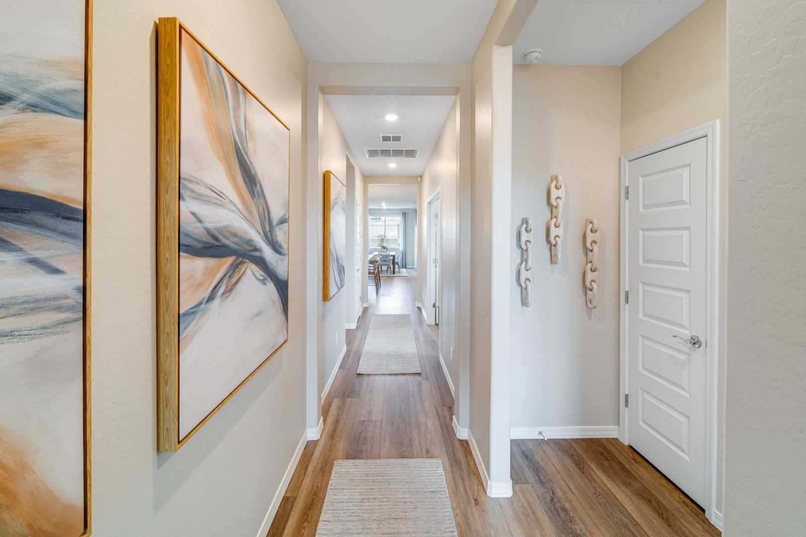 Spacious hallway in The Newport B home design featuring hardwood floors, beige walls, abstract artwork, and open doors