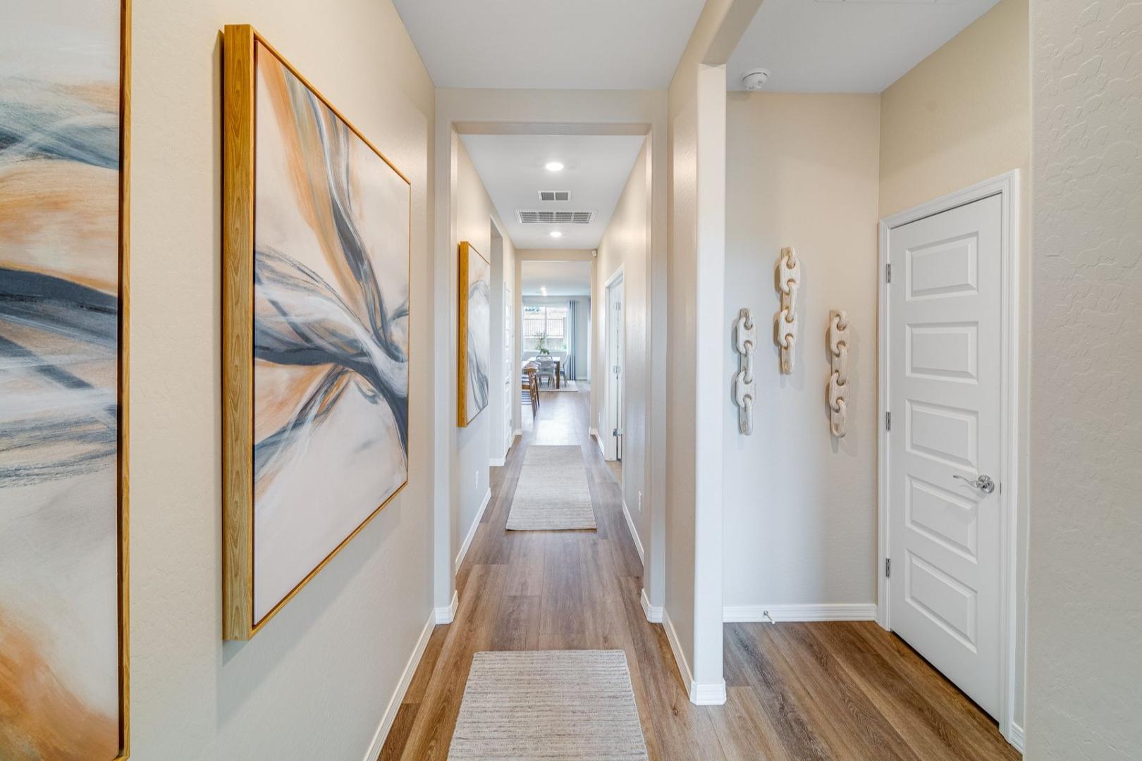 Spacious hallway in The Newport C home with hardwood floors, beige walls, abstract gold-framed art, and white doors