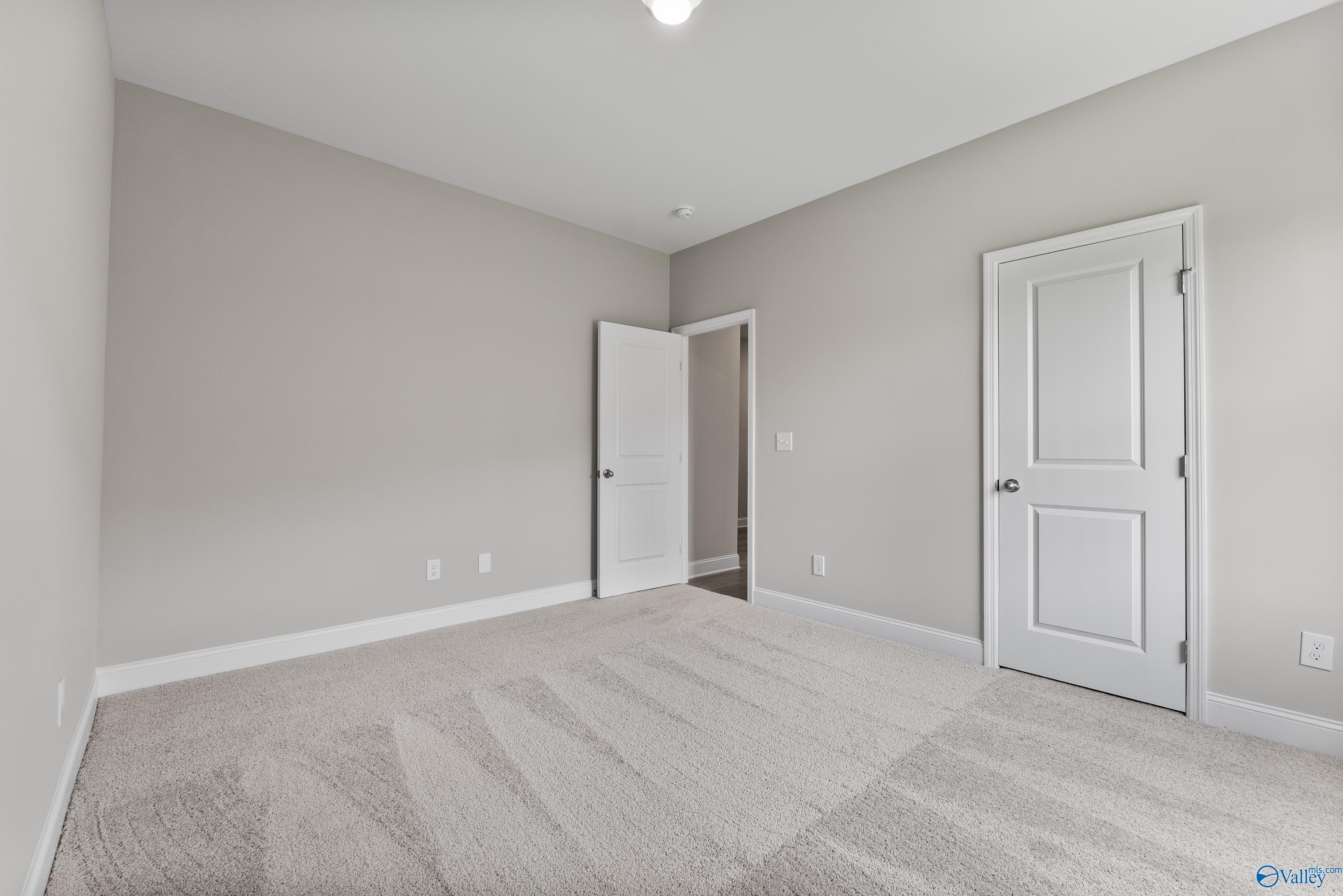 Bright secondary bedroom with neutral beige walls, white doors, and plush carpet in Davidson Homes The Daphne C, Harvest, Alabama