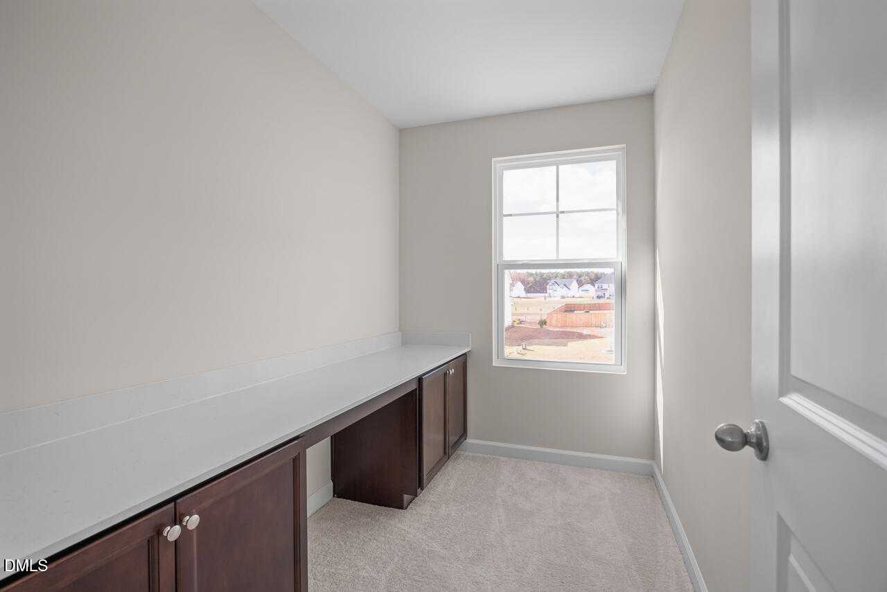 Bright home office with built-in desk, dark cabinets, large window, and neutral walls in Davidson Homes The Gavin C, Lillington, NC