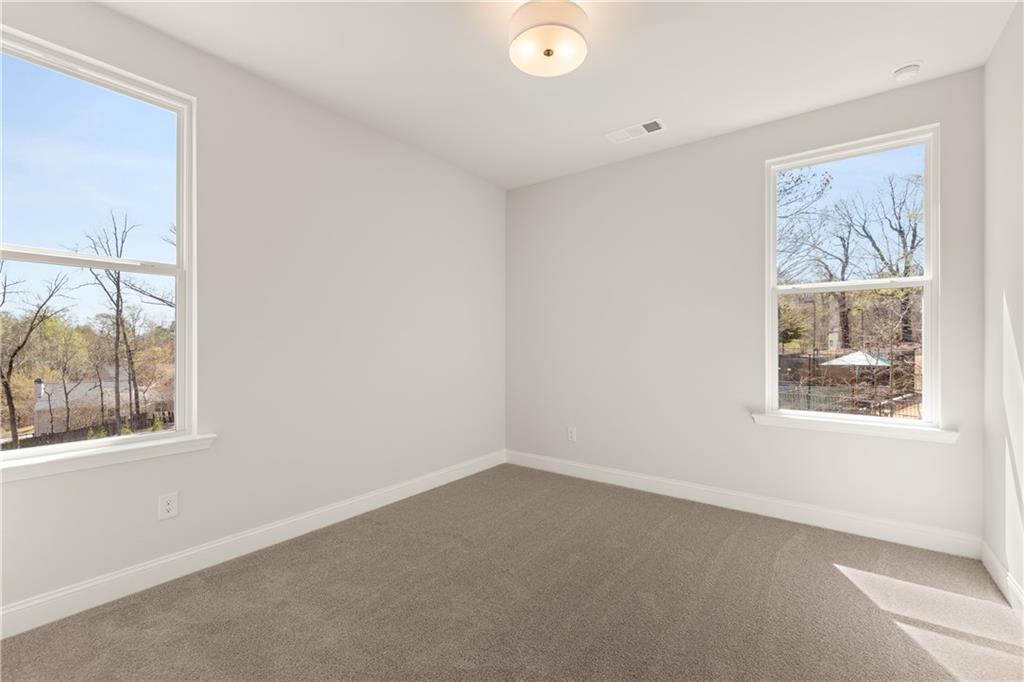 Bright bedroom with light gray walls, beige carpet, large windows overlooking wooded backyard in The Danbury C, Buford, GA