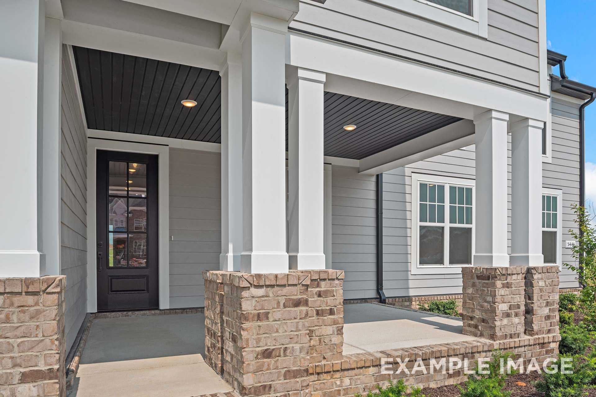 Spacious front porch of The Hathaway home with white columns, black glass door, gray siding, and brick accents by Davidson Homes