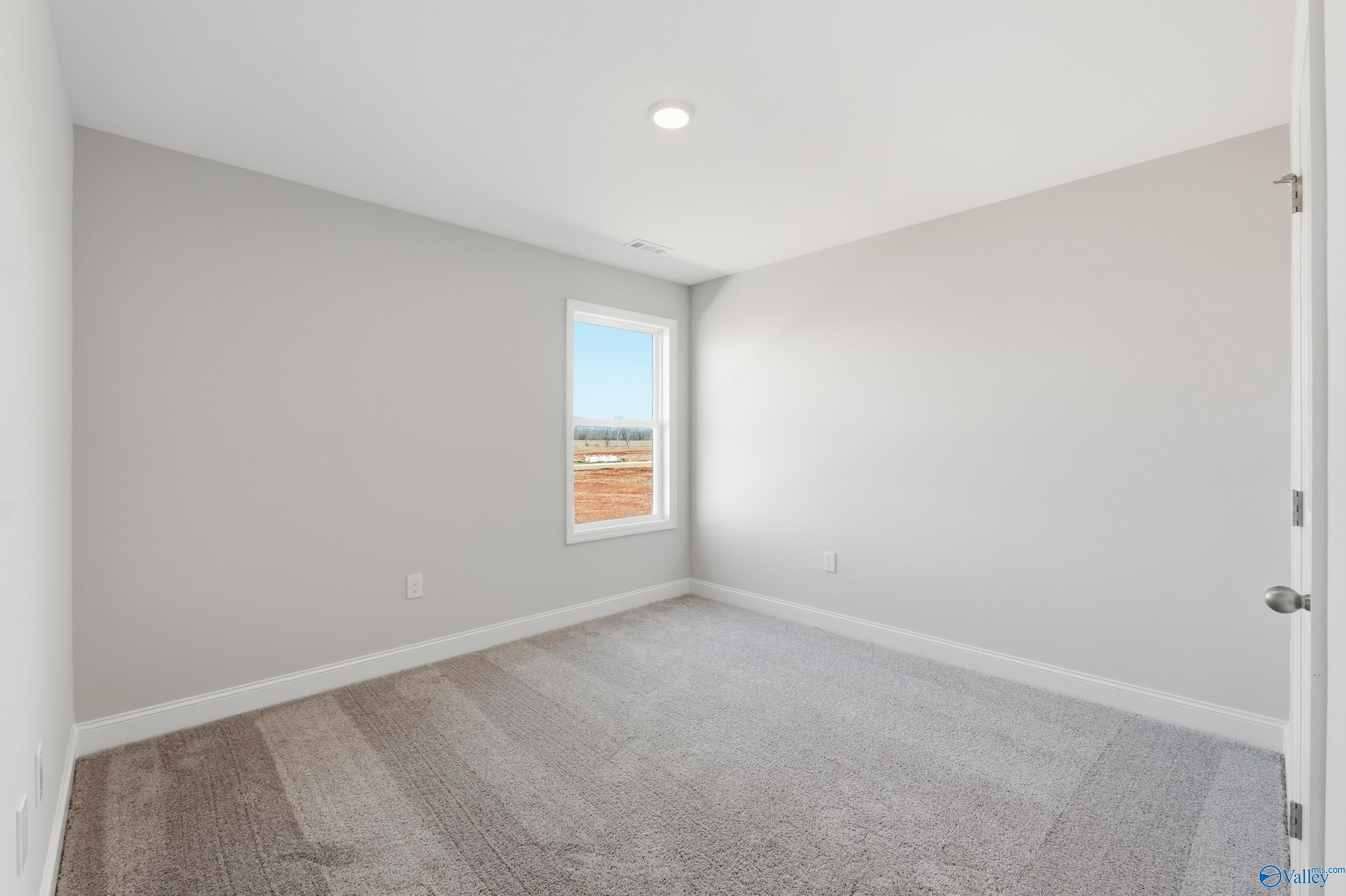 Bright secondary bedroom featuring gray walls, neutral carpet, and large window in Davidson Homes The Franklin, Heritage Lakes, New Market, Alabama