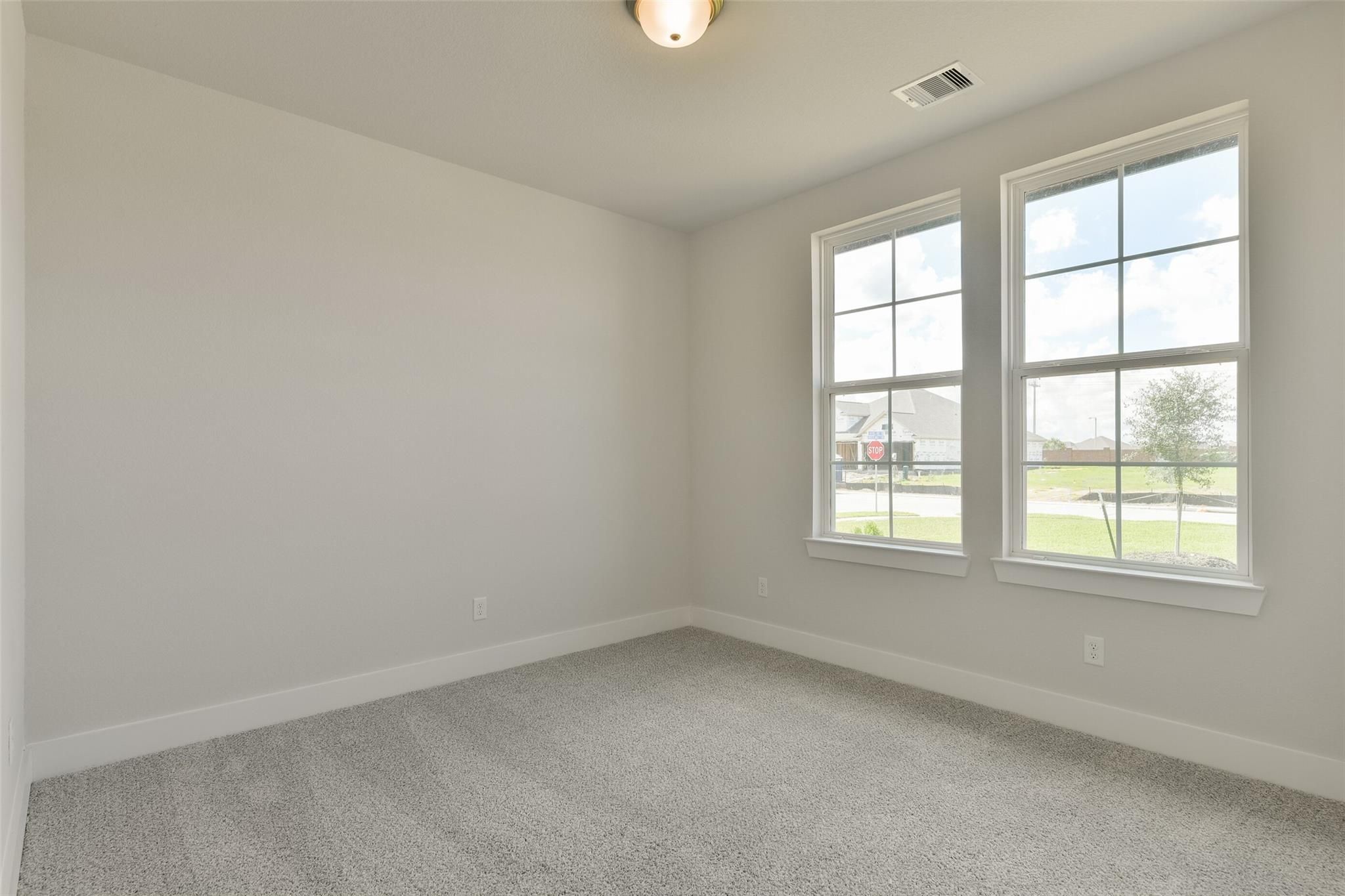 Bright secondary bedroom with beige walls, gray carpet, and large windows overlooking yard in Davidson Homes The Edward A, Lago Mar