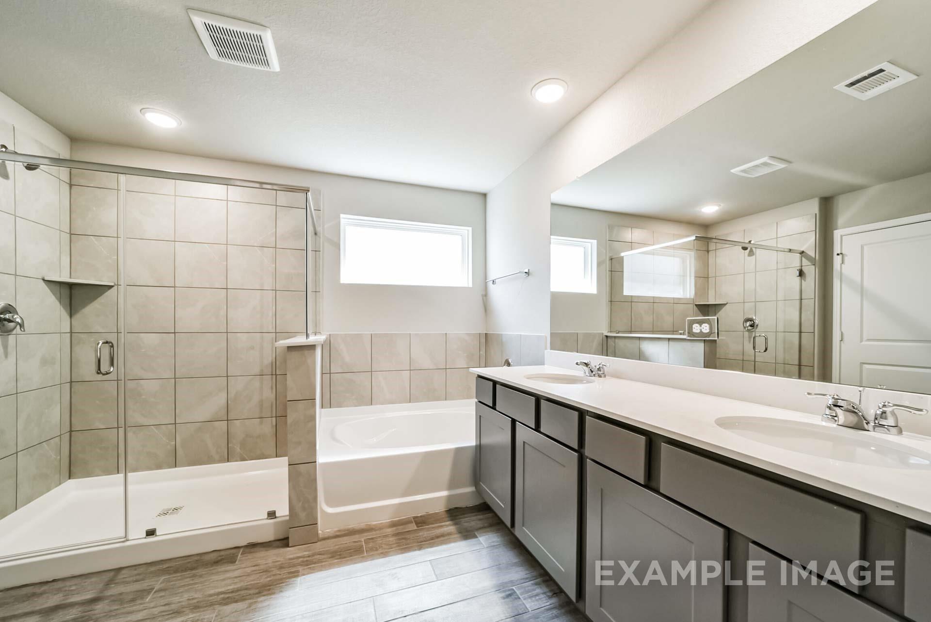 Primary bathroom with dual vanity, soaking tub, and walk-in glass shower in The Riviera A home at Emberly in Beasley, TX.