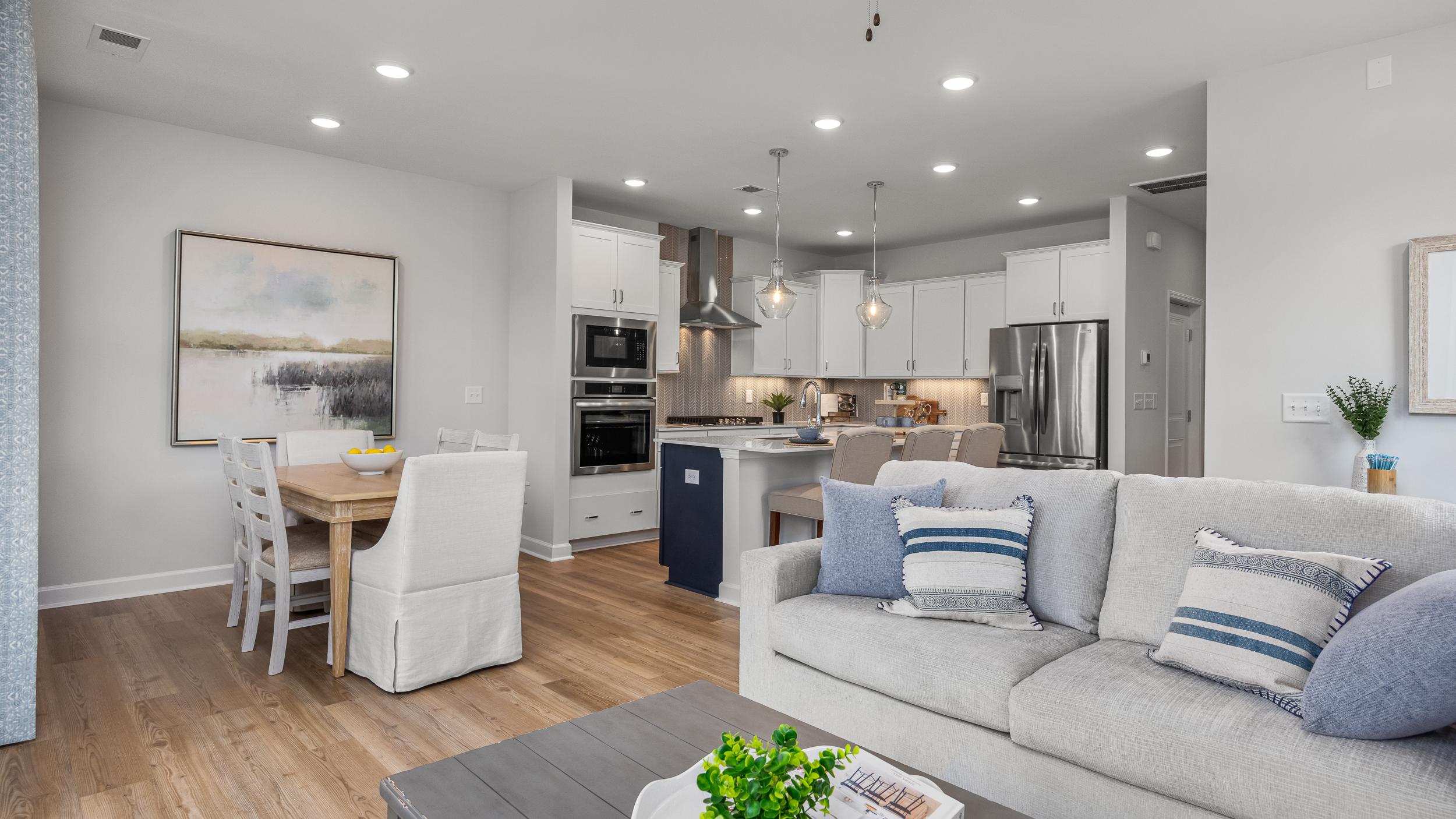 Open-concept kitchen and living room in Springvale Fuquay-Varina NC by Davidson Homes featuring white cabinets hardwood floors and gray sofa