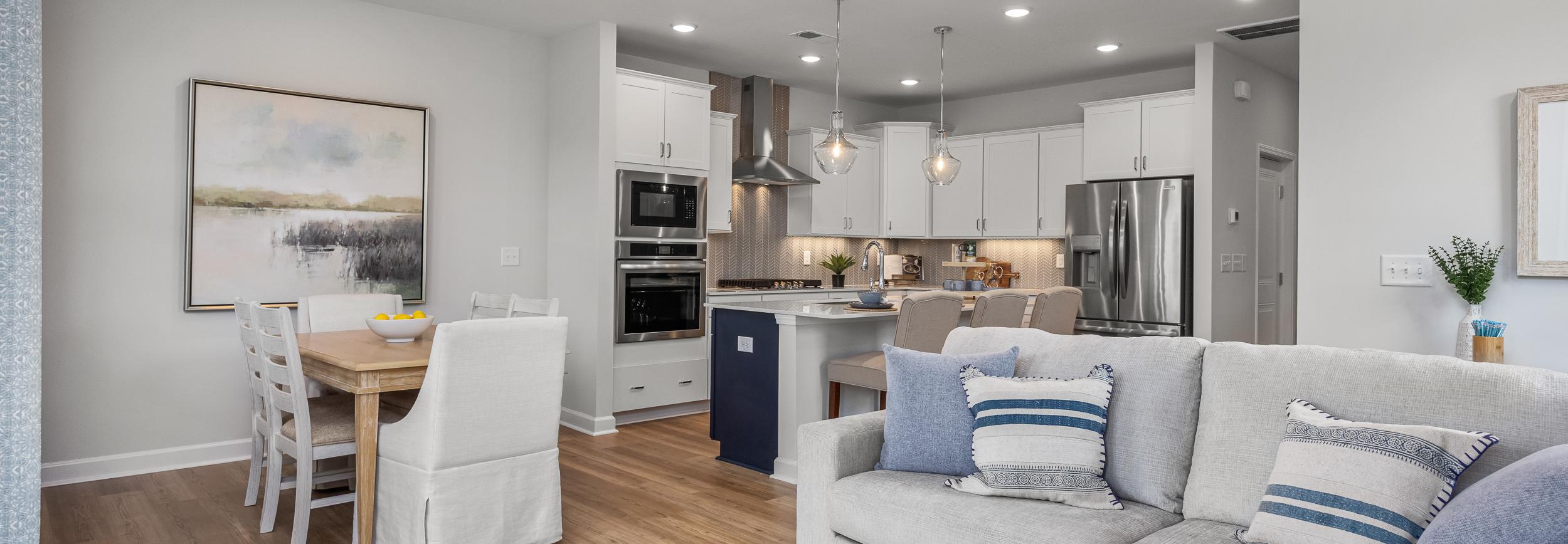 Open-concept kitchen and living room in Springvale Fuquay-Varina NC by Davidson Homes featuring white cabinets hardwood floors and gray sofa