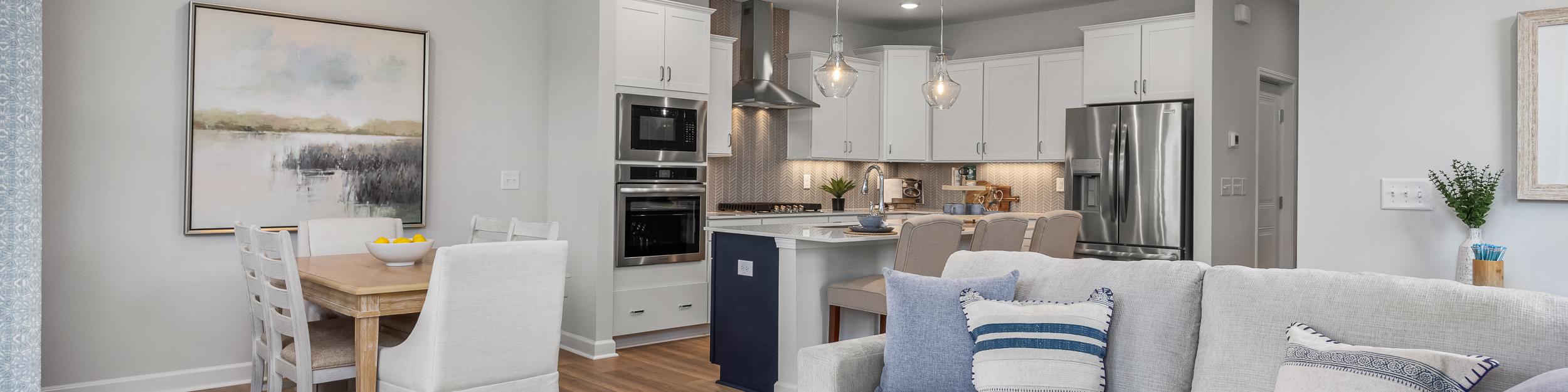 Open-concept kitchen and living room in Springvale Fuquay-Varina NC by Davidson Homes featuring white cabinets hardwood floors and gray sofa