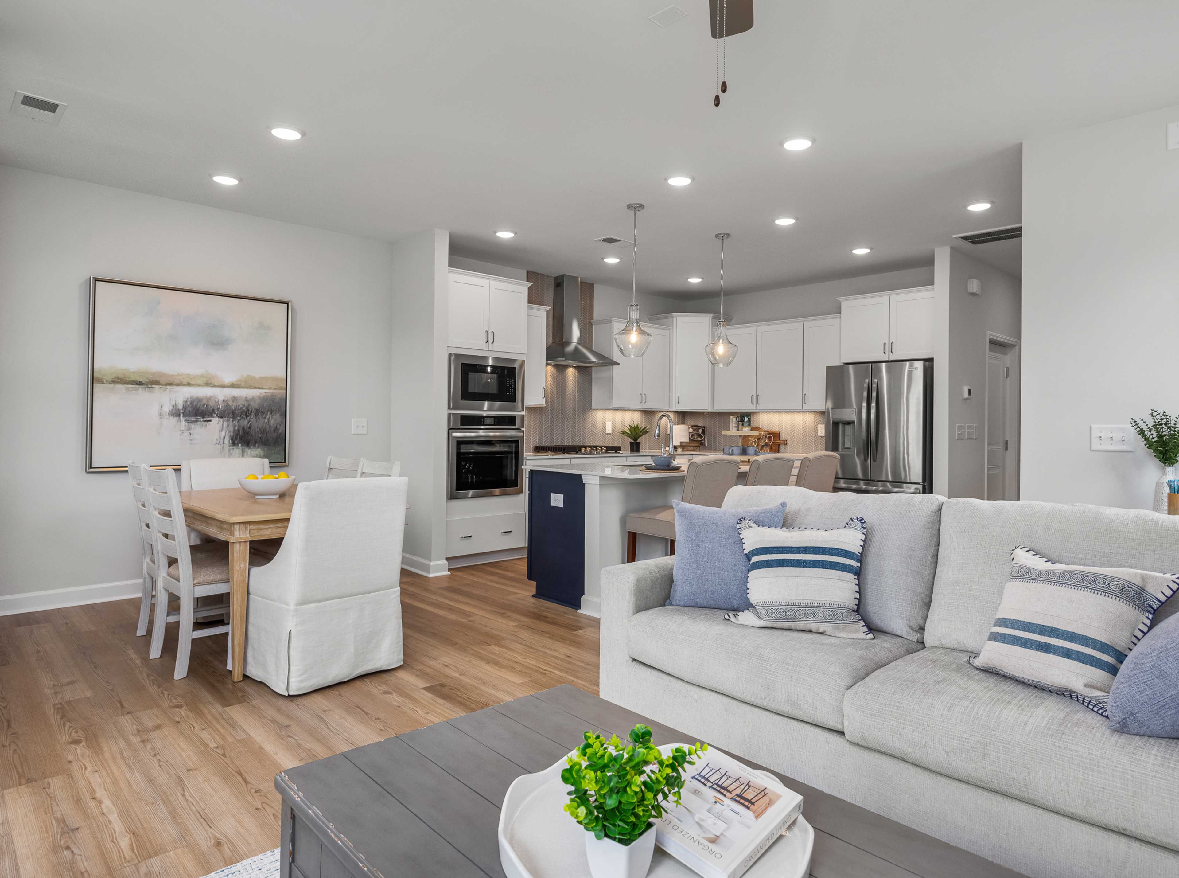 Open-concept kitchen and living room in Springvale Fuquay-Varina NC by Davidson Homes featuring white cabinets hardwood floors and gray sofa