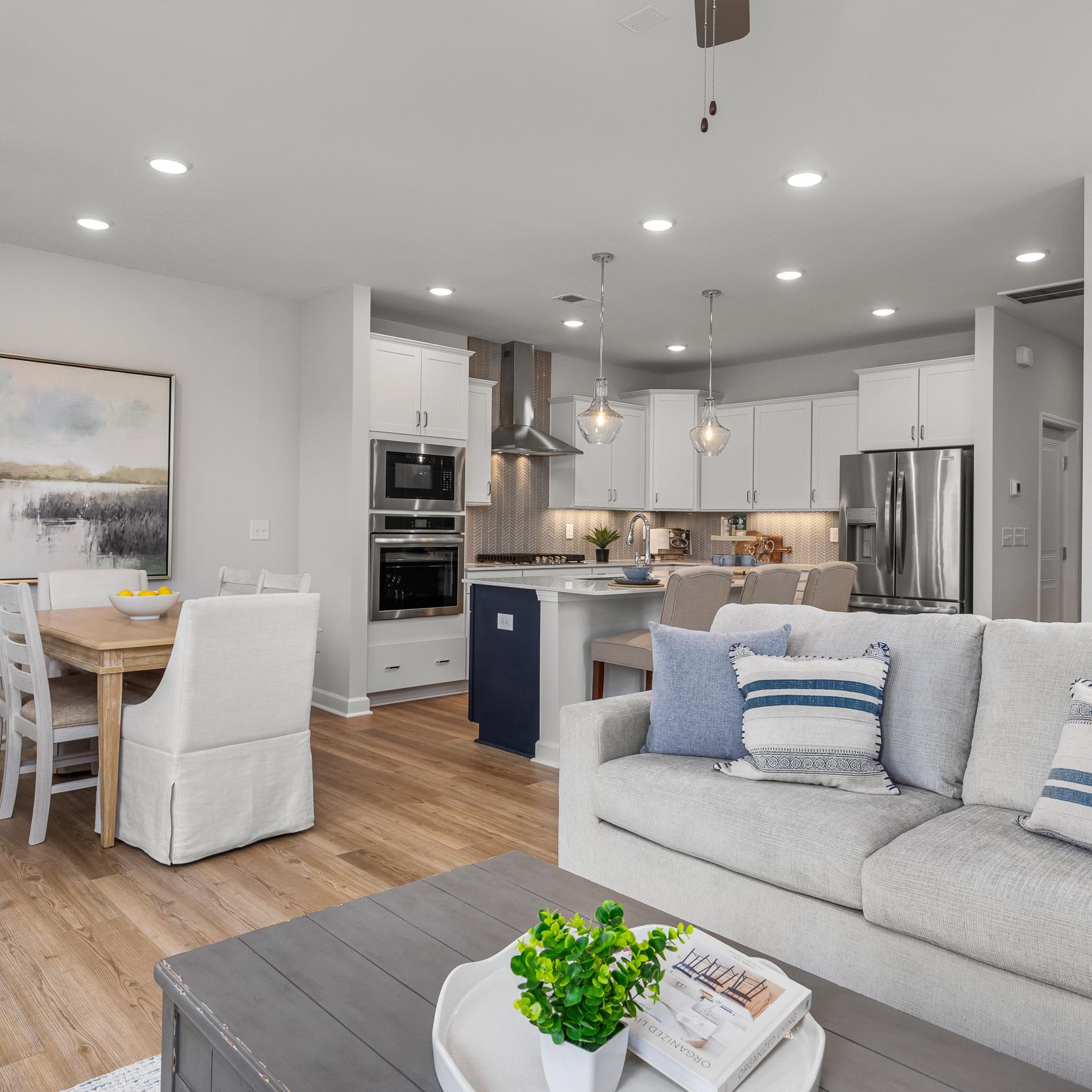 Open-concept kitchen and living room in Springvale Fuquay-Varina NC by Davidson Homes featuring white cabinets hardwood floors and gray sofa