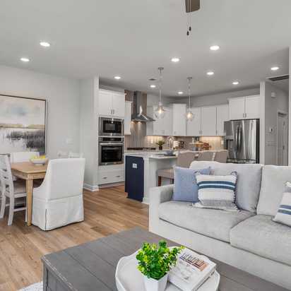 Open-concept kitchen and living room in Springvale Fuquay-Varina NC by Davidson Homes featuring white cabinets hardwood floors and gray sofa
