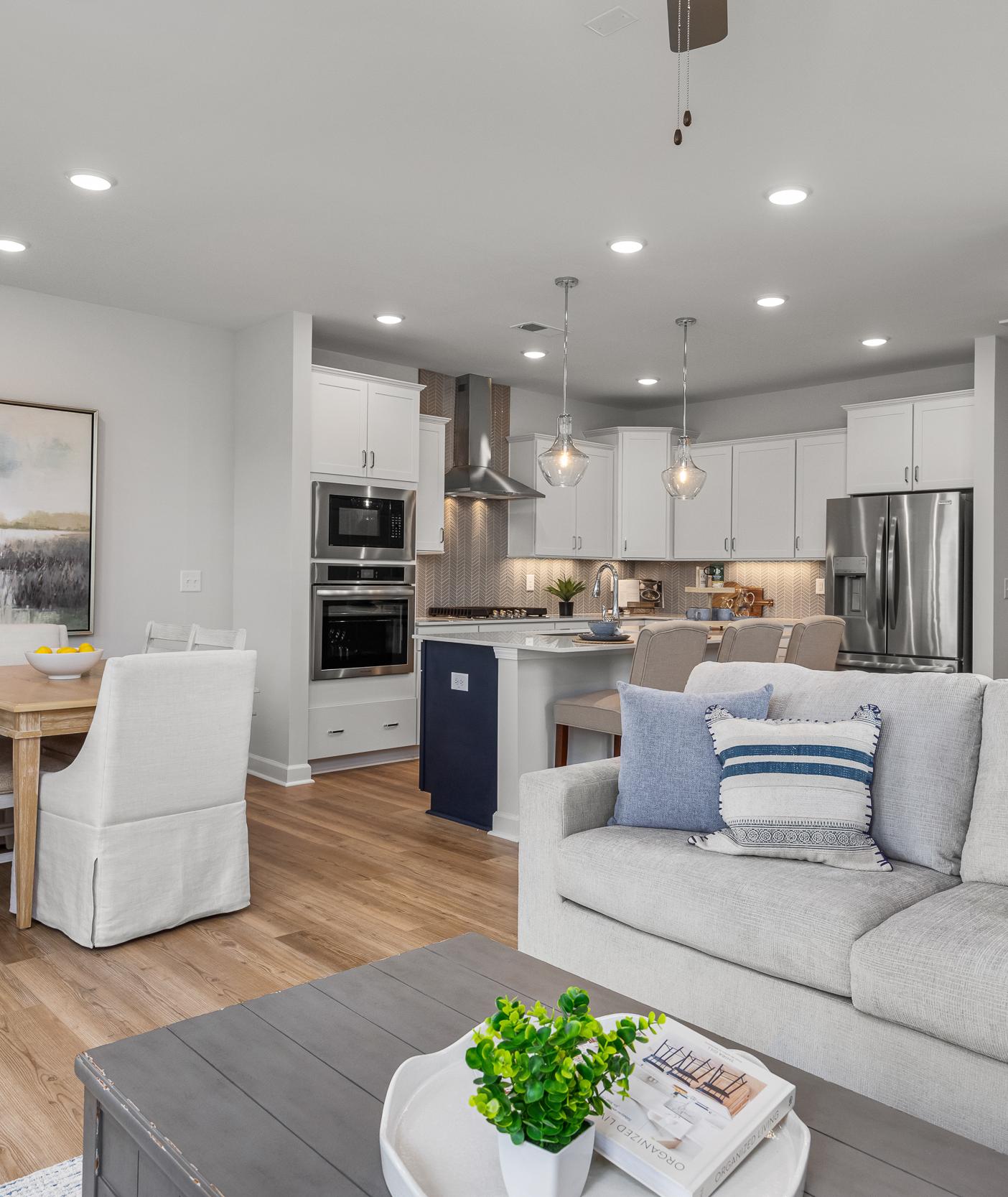 Open-concept kitchen and living room in Springvale Fuquay-Varina NC by Davidson Homes featuring white cabinets hardwood floors and gray sofa