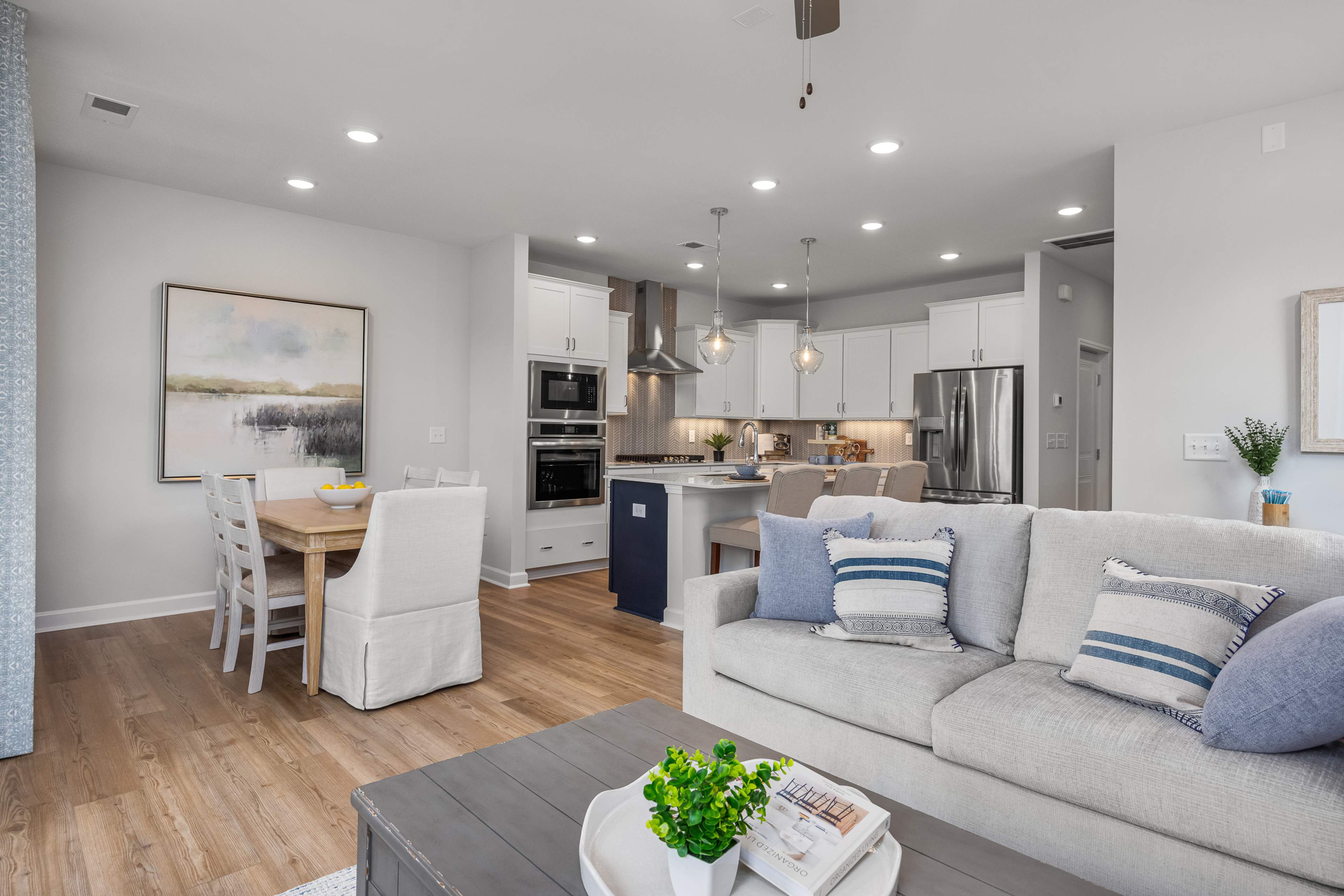 Open-concept kitchen and living room in Springvale Fuquay-Varina NC by Davidson Homes featuring white cabinets hardwood floors and gray sofa