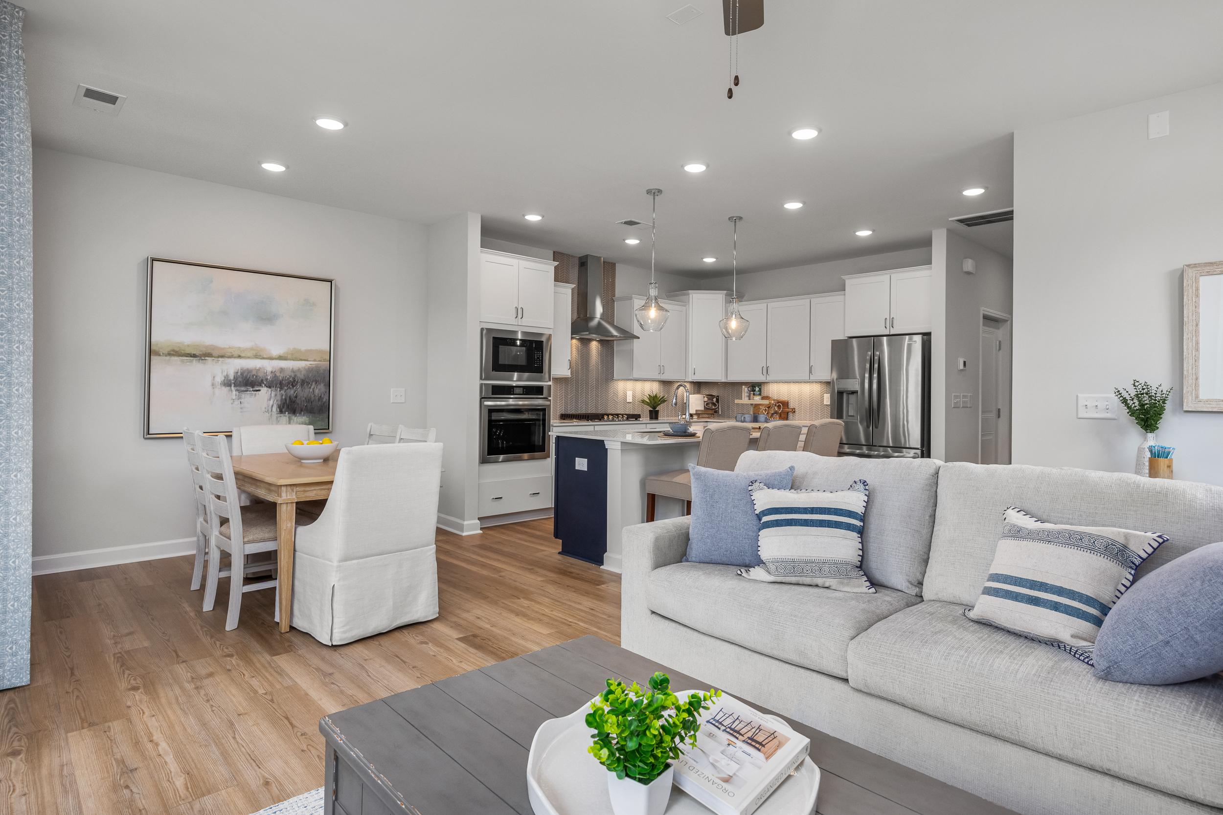 Open-concept living and kitchen in Springvale home, Fuquay-Varina NC with hardwood floors, white cabinets, gray sofa, and modern island