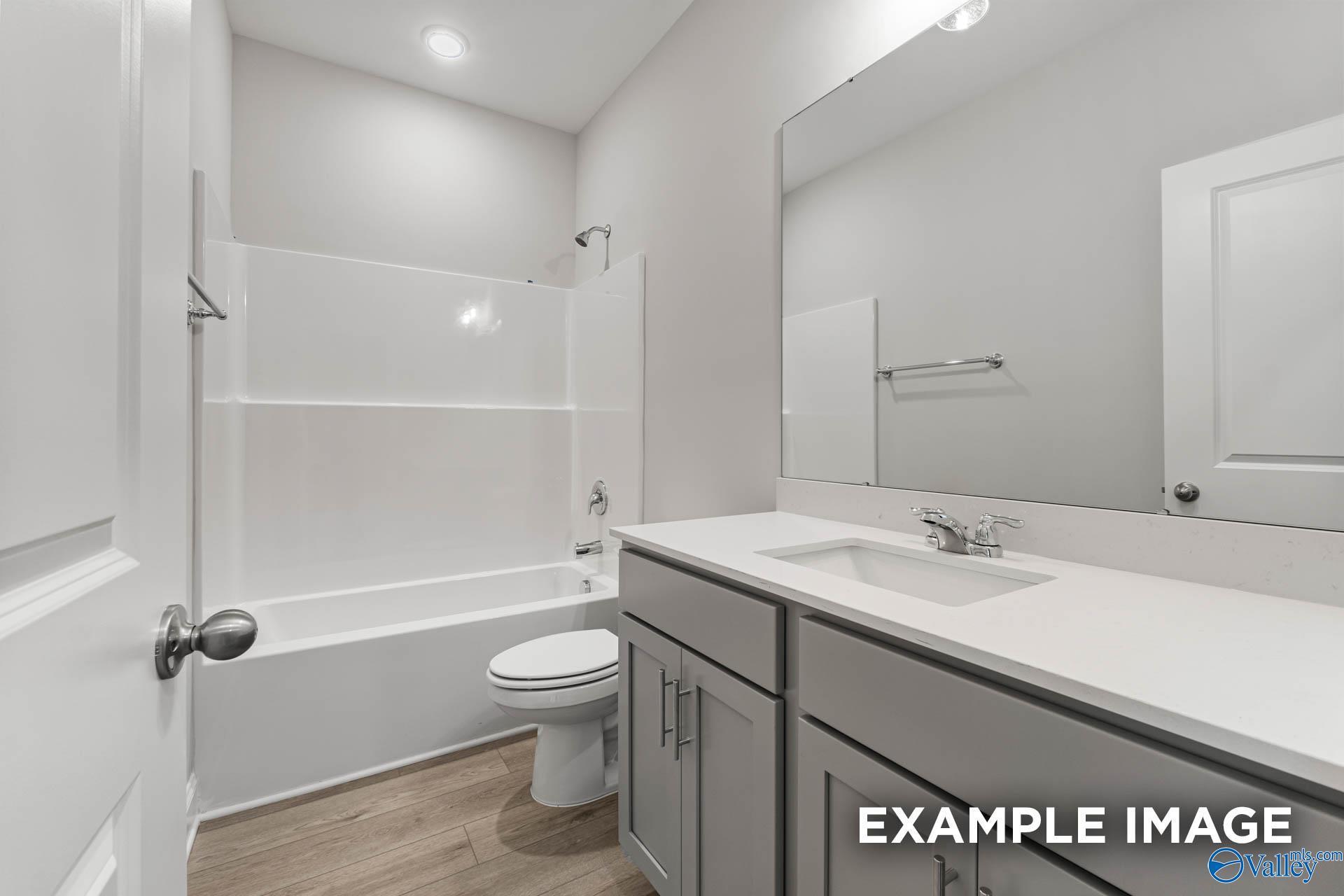 Modern bathroom with white tub-shower combo, gray vanity, toilet and mirror in 4-bed Davidson Homes The Daphne, Hazel Green, AL