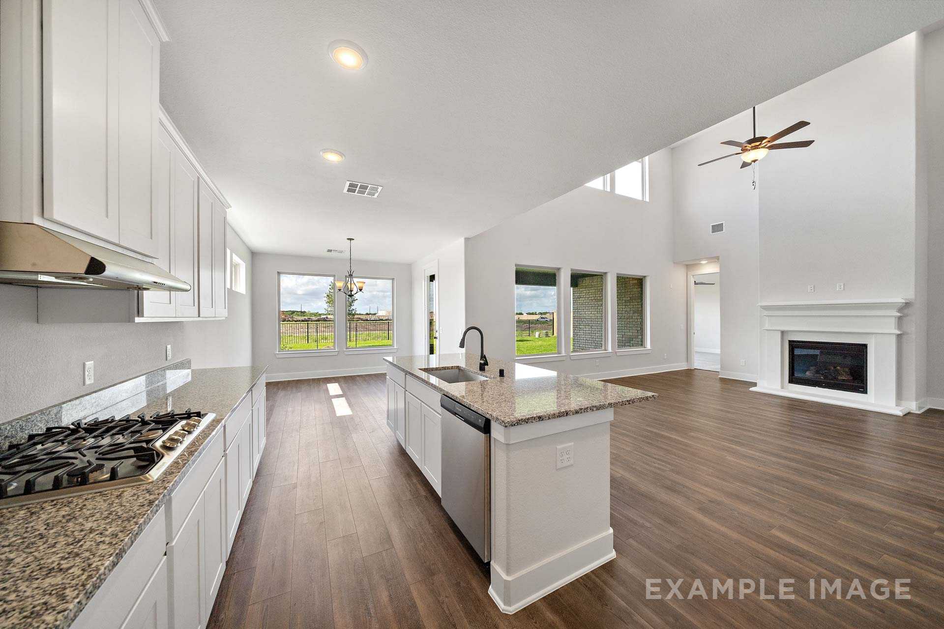 Spacious open-concept kitchen in The Victoria A with white shaker cabinets, granite island, gas range, and adjacent living area featuring fireplace