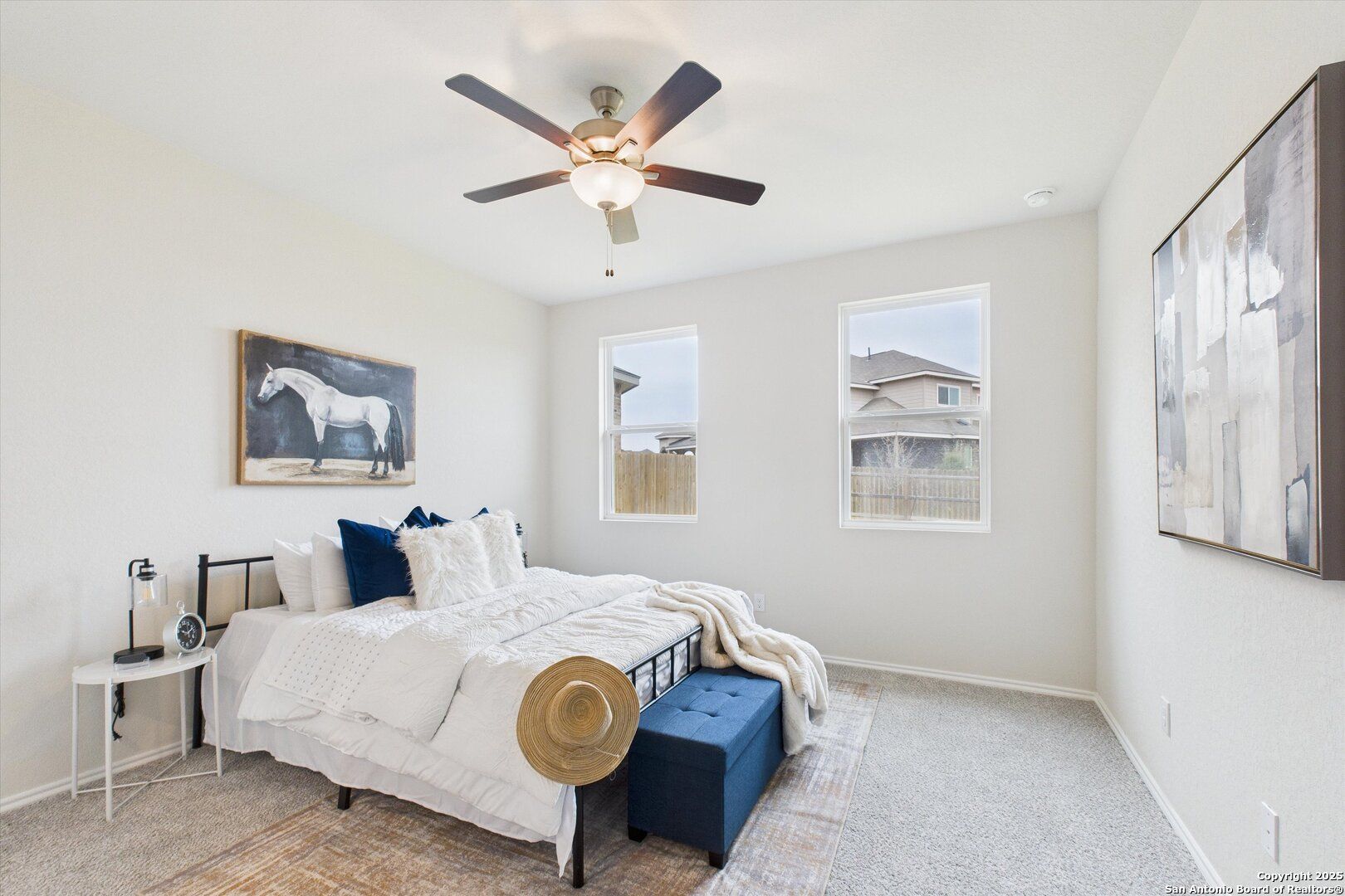 Serene master bedroom with white duvet, blue pillows, ceiling fan, and large windows in Davidson Homes The Asheville K, Bricewood, San Antonio