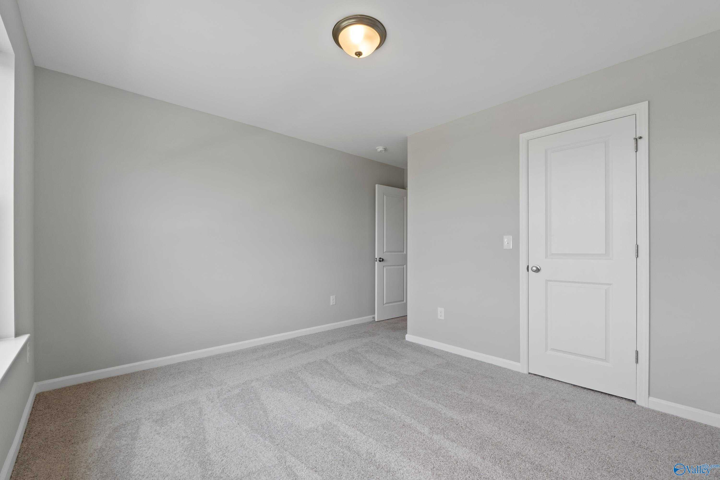 Empty secondary bedroom featuring gray walls, plush carpet, white doors, and ceiling light in Davidson Homes The Dorado, Athens AL