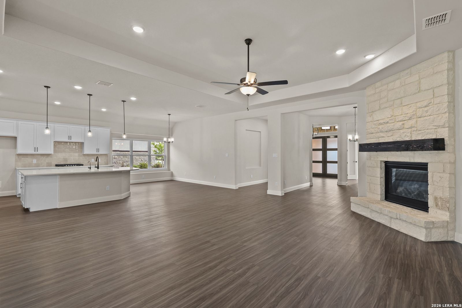 Open-concept living room and kitchen with stone fireplace in The Summerlin B floor plan by Davidson Homes, Castroville, TX.