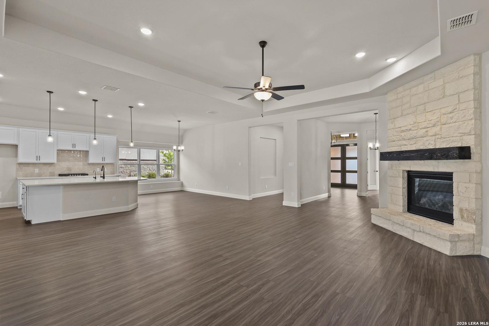 Open-concept living room and kitchen with stone fireplace in The Summerlin B floor plan by Davidson Homes, Castroville, TX.