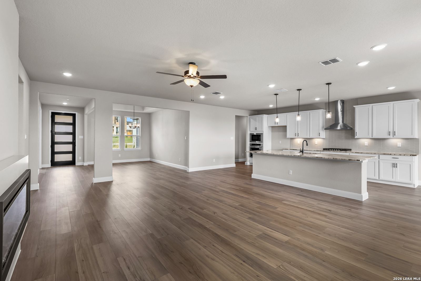 Open-concept living room and kitchen with white cabinets, island, and wood-look flooring in Davidson Homes Foster E, Castroville, TX