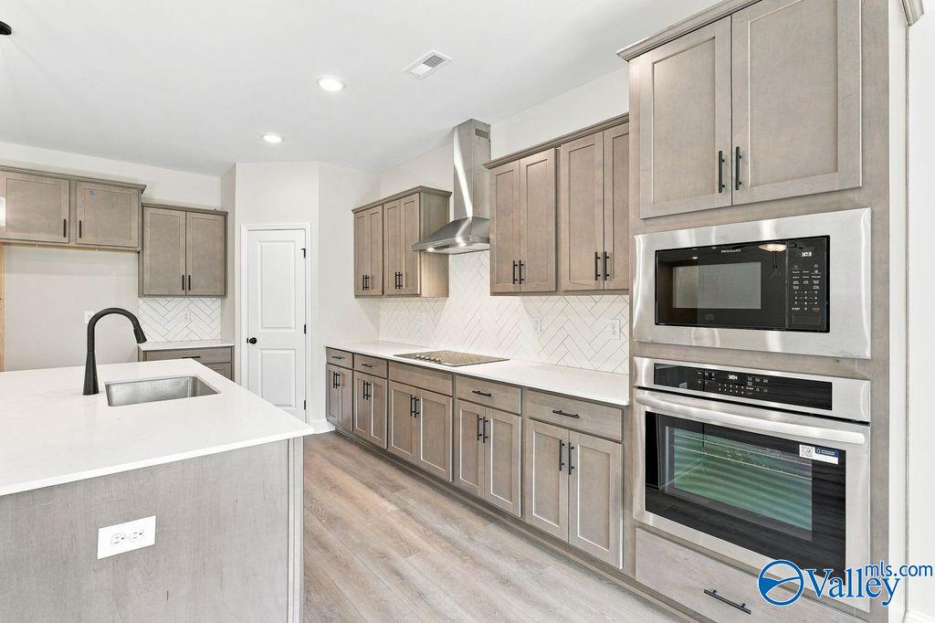 Modern kitchen with greige cabinets, herringbone backsplash, and stainless appliances in Davidson Homes The Rockford, Hartselle, Alabama
