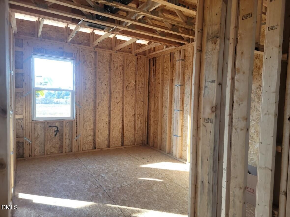 Framed bedroom with wooden studs, large window, exposed beams, and plywood floor in Davidson Homes The Willow G, Angier, NC