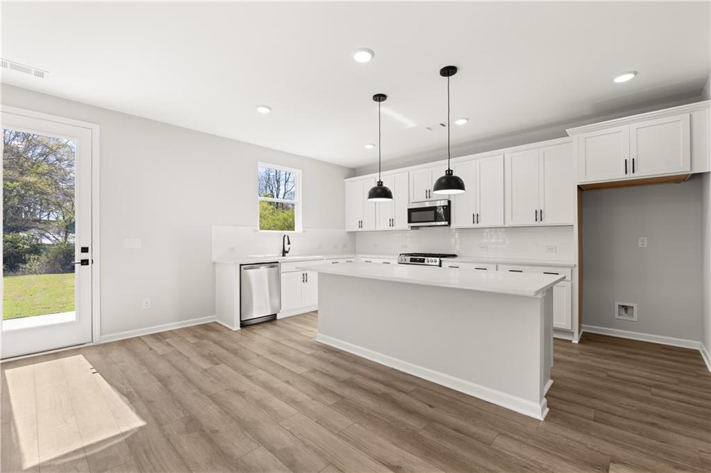 Modern white kitchen with island, stainless steel appliances, pendant lights, and backyard view in The Hickory B, Winder, GA