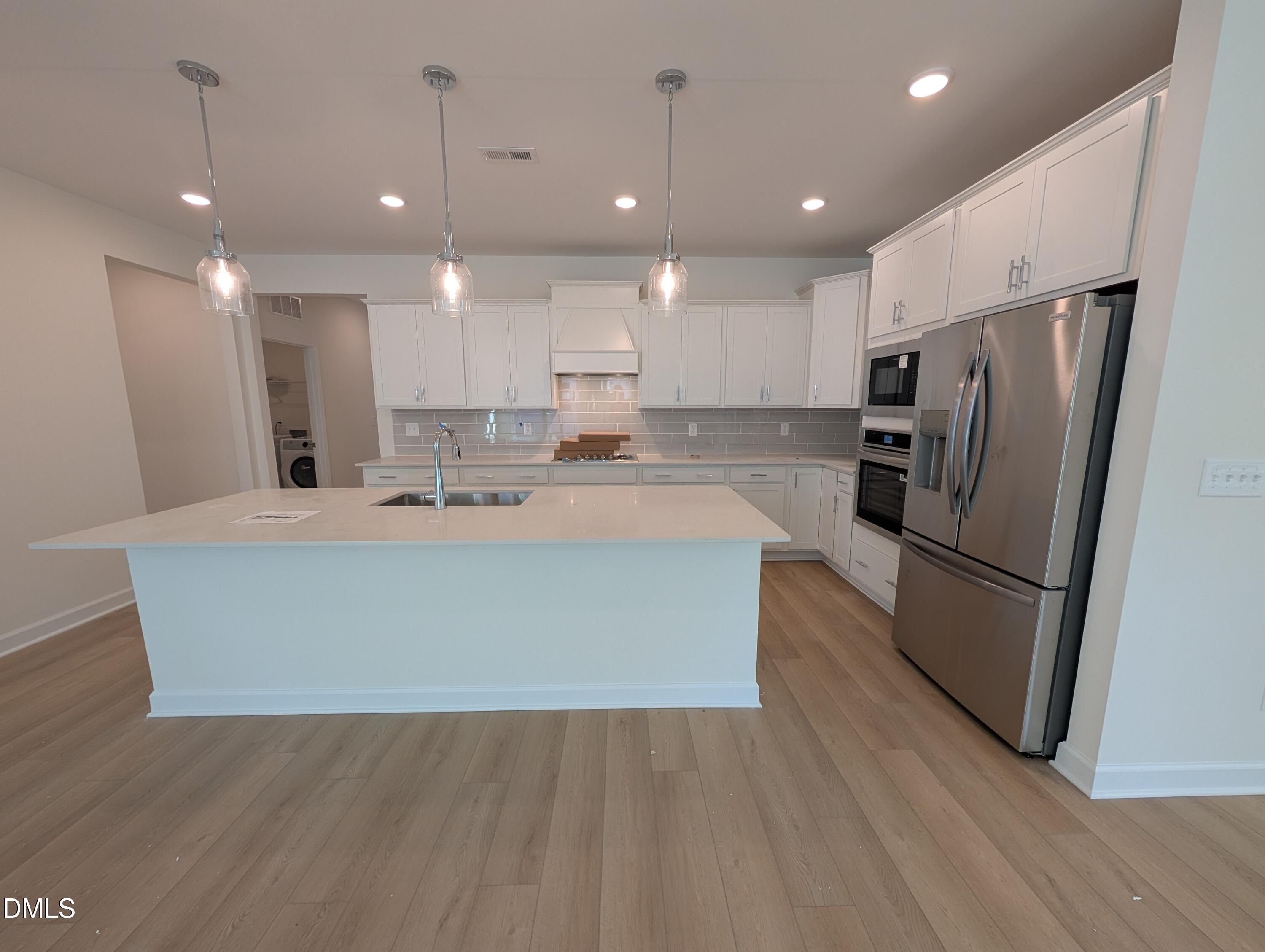 Bright white kitchen with large island, pendant lights, stainless appliances, and luxury vinyl plank flooring in Davidson Homes' The Magnolia A, Wendell Ridge.