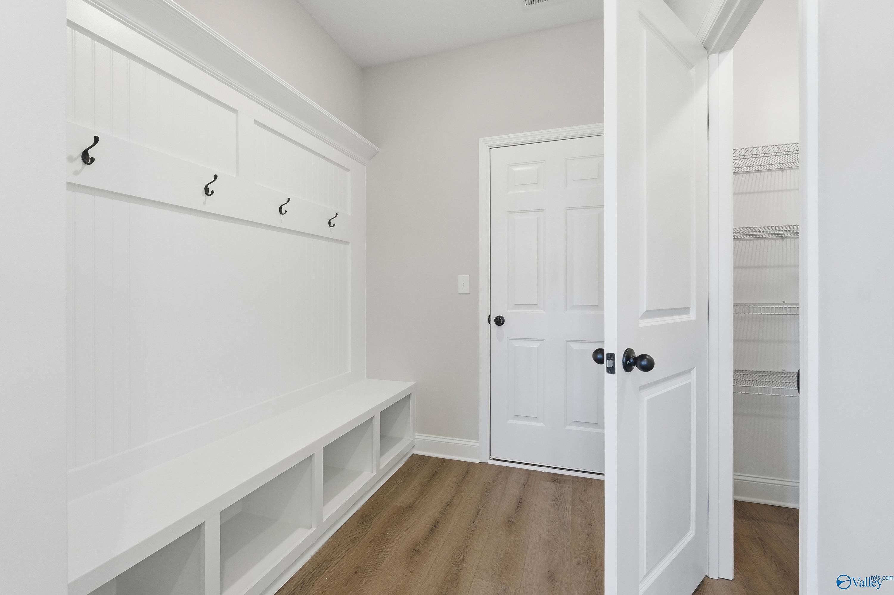 White built-in mudroom with lockers, wall hooks, storage bench, and laundry access in Davidson Homes The Chelsea C, Harvest, Alabama