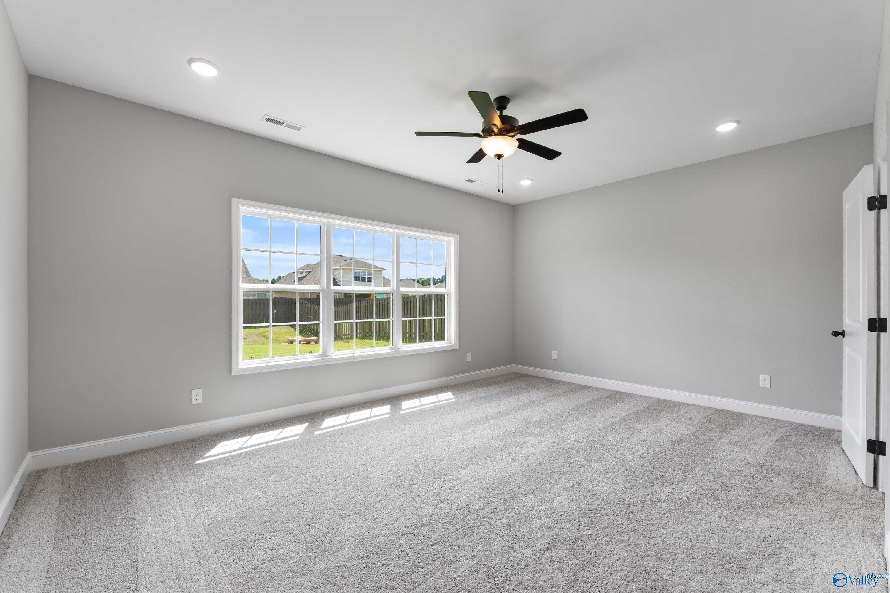 Bright bonus room with ceiling fan, large window overlooking green yard, gray walls and carpet in Davidson Homes The Montgomery B With Bonus, Toney, AL
