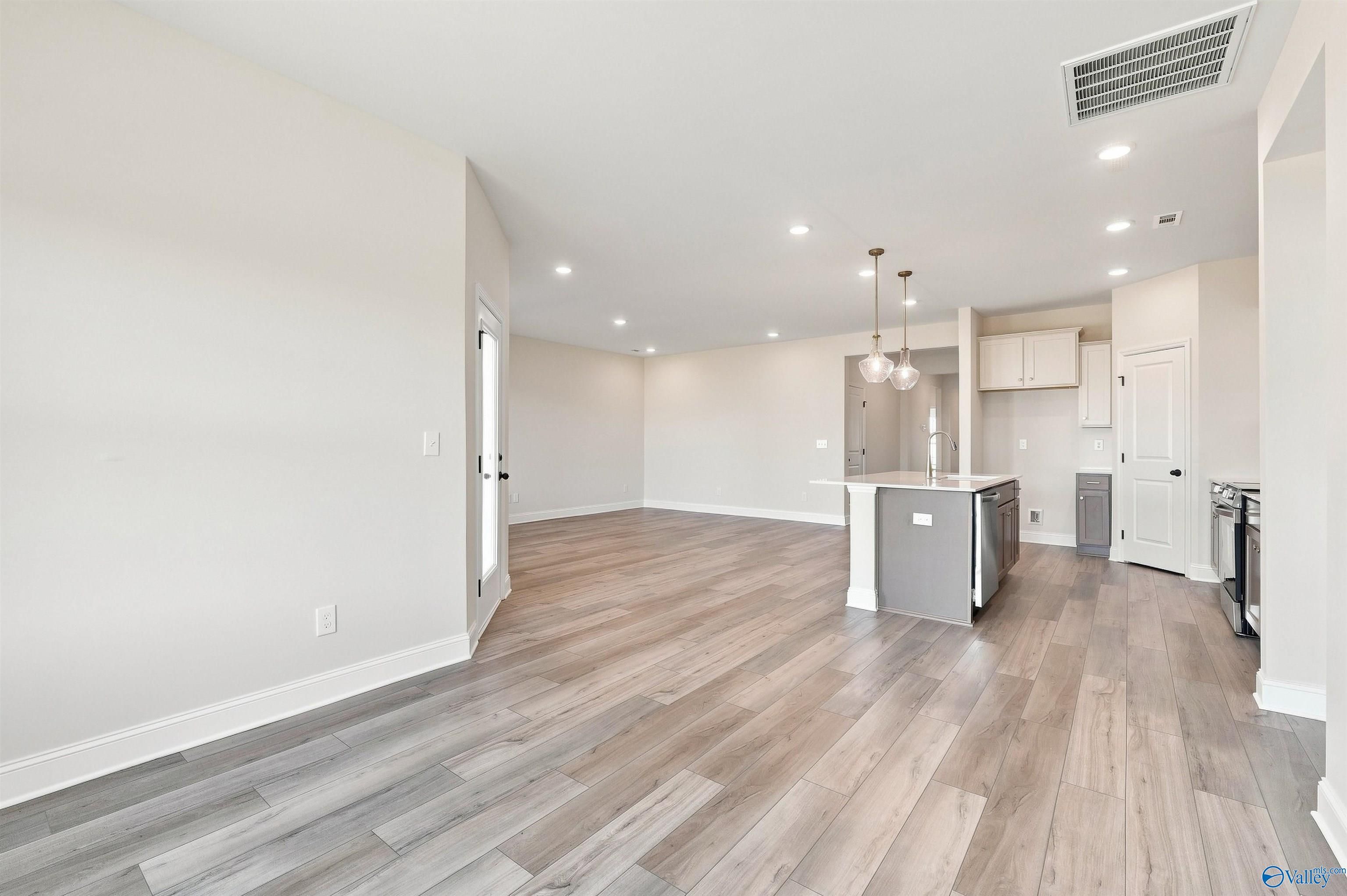 Open-concept living area with gray kitchen island and luxury vinyl plank flooring in The Everett B, Ivy Hills, Toney, Alabama