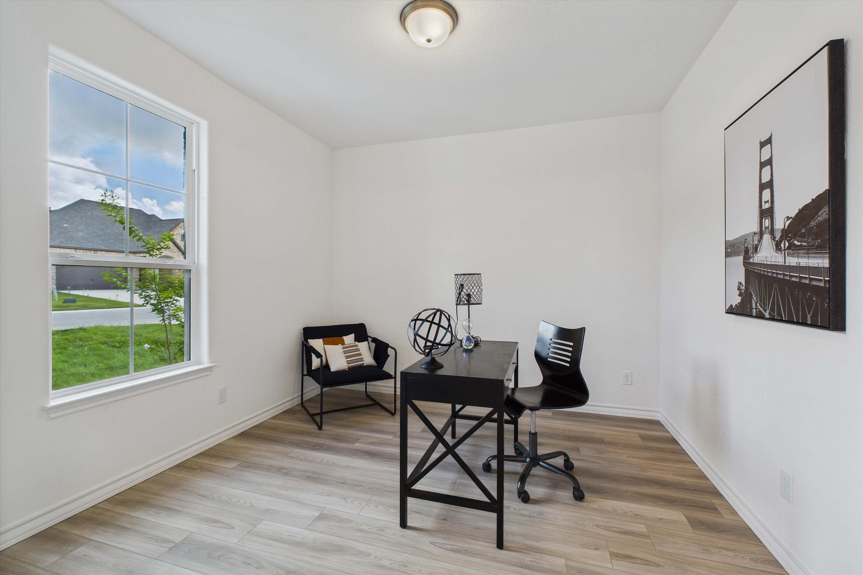 Modern home office in The Danbury featuring a black desk, accent chair, wood-look flooring, and natural light.
