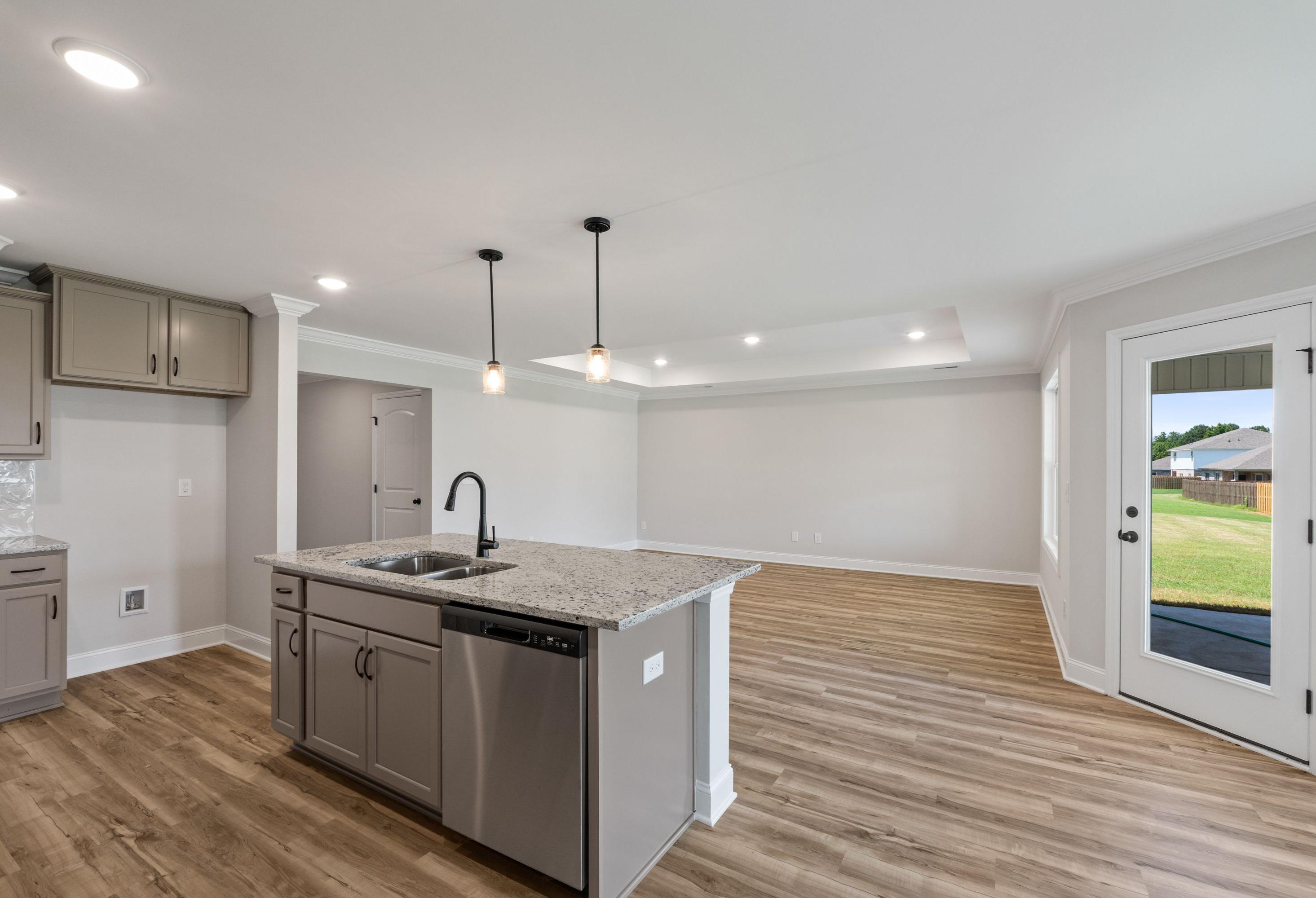 Open-concept kitchen in The Holly C featuring a granite island, pendant lighting, and view of the living area.