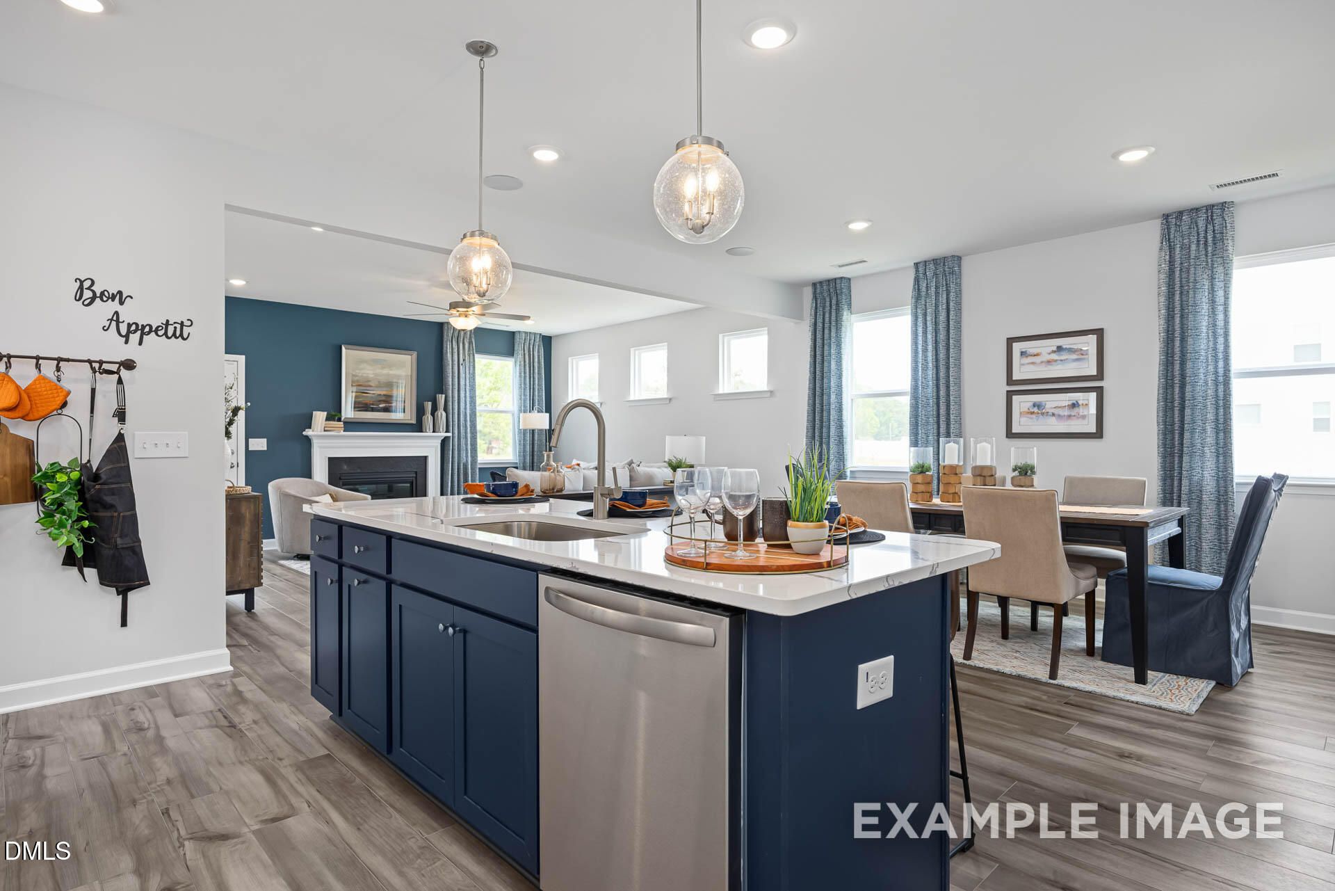 Modern kitchen with dark blue island, stainless appliances, and open dining area in The Adalynn A, Woodland Crossing, Zebulon.