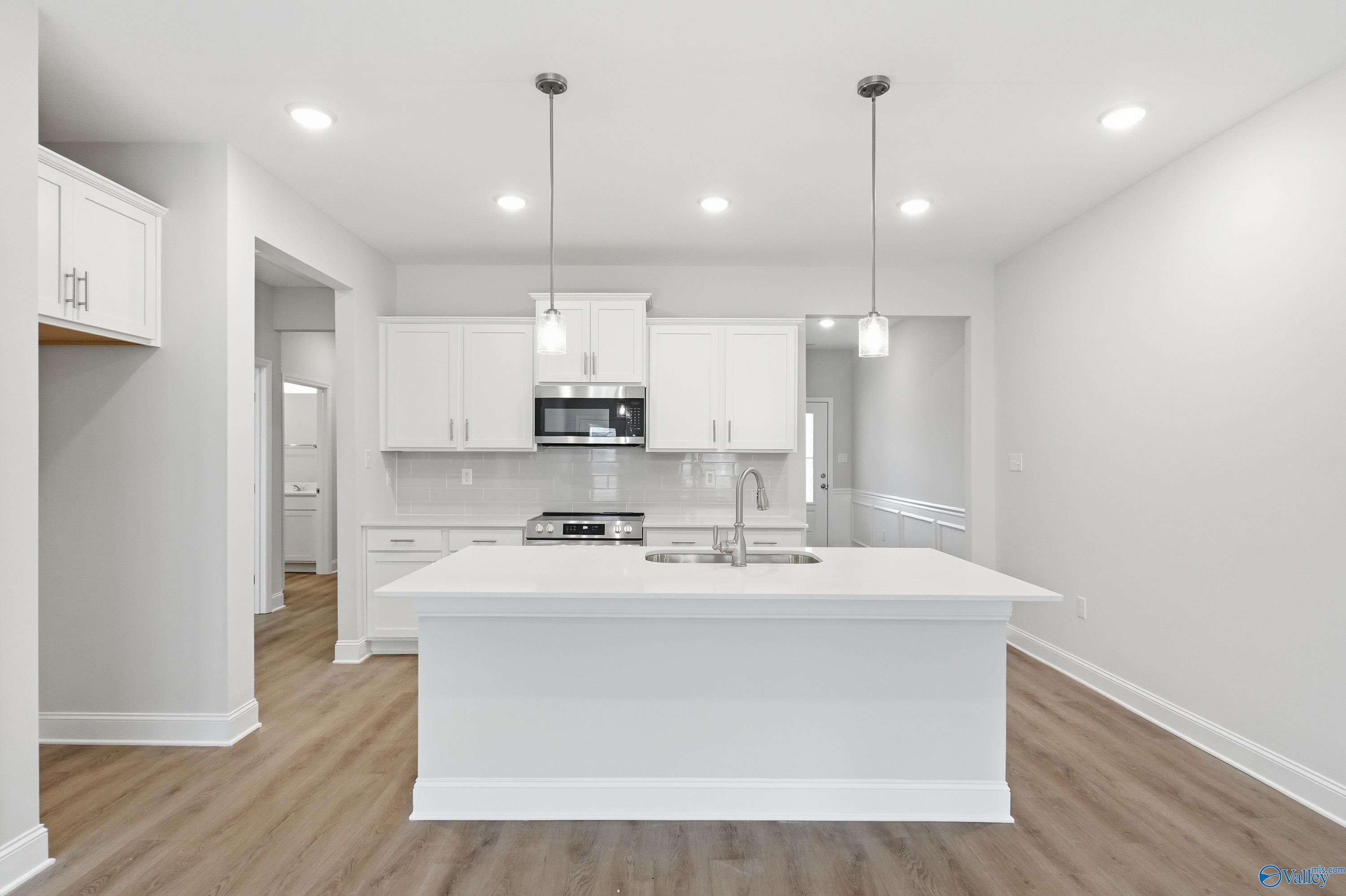 Modern white kitchen island with sink, stainless appliances, and pendant lights in Davidson Homes The Cumberland, Decatur AL