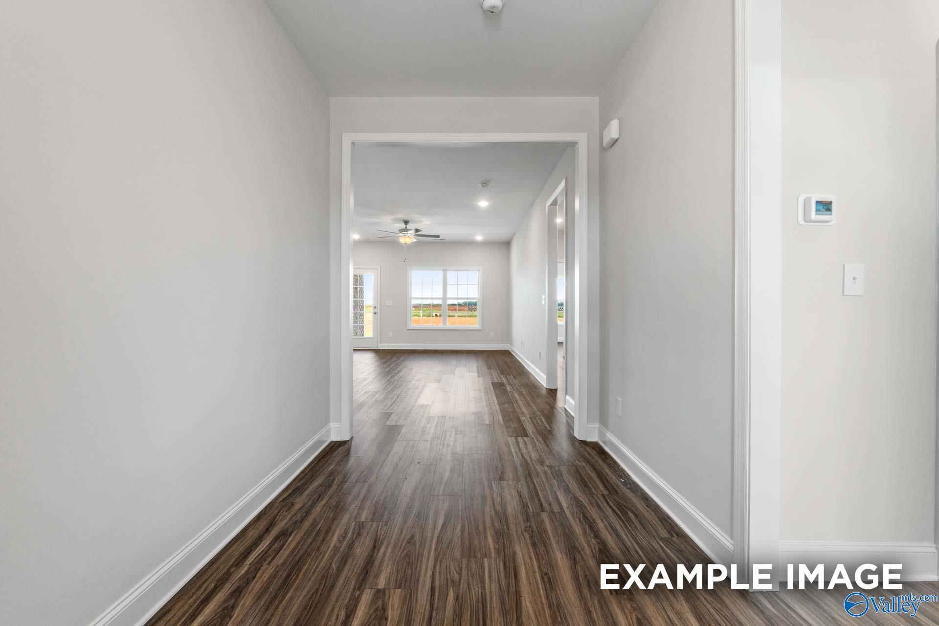 Spacious hallway with light gray walls and dark hardwood floors opening to bright room with large windows in The Montgomery home, Hartselle, AL