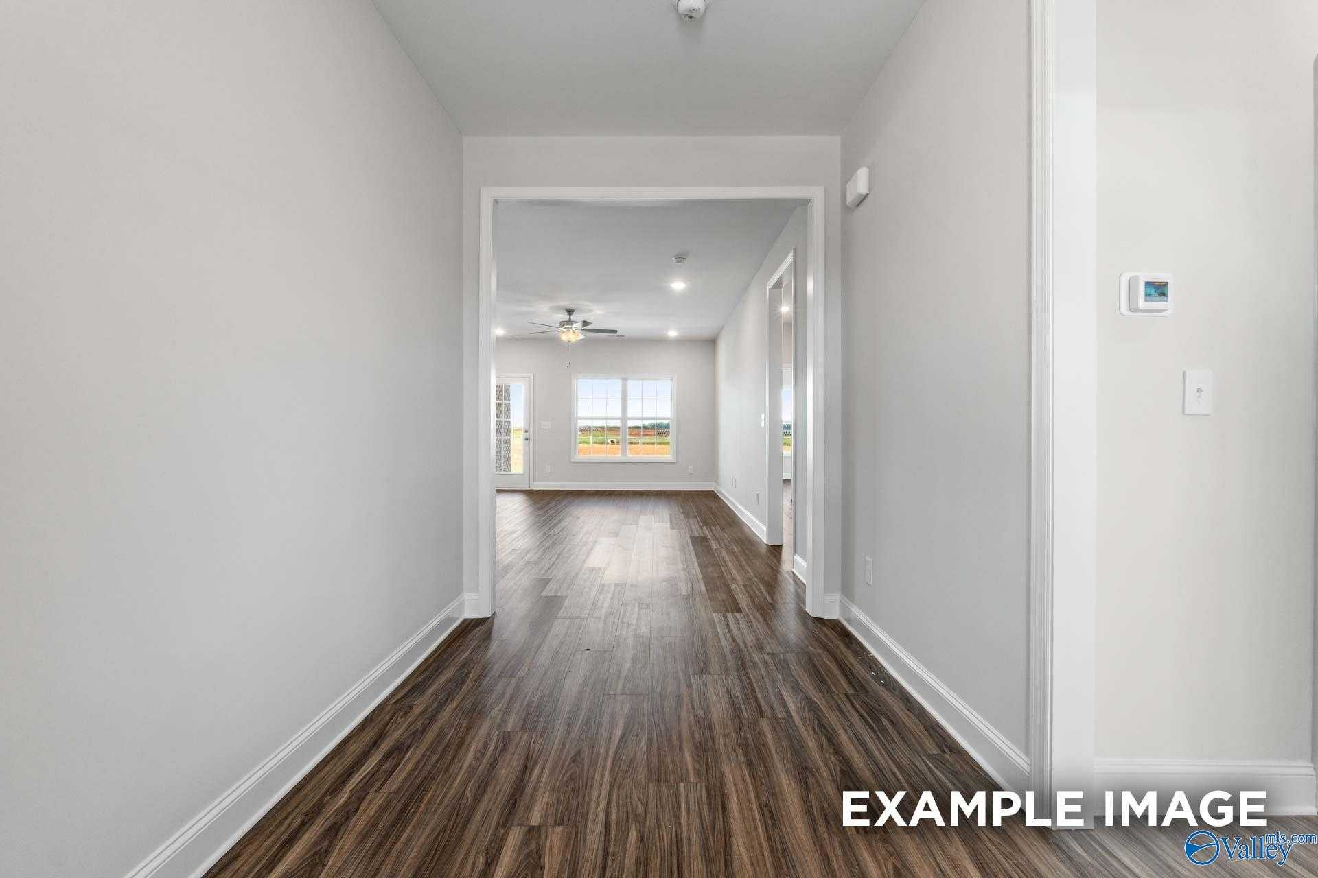 Bright hallway with dark hardwood floors and neutral walls opening to sunlit room in The Montgomery by Davidson Homes, Athens AL