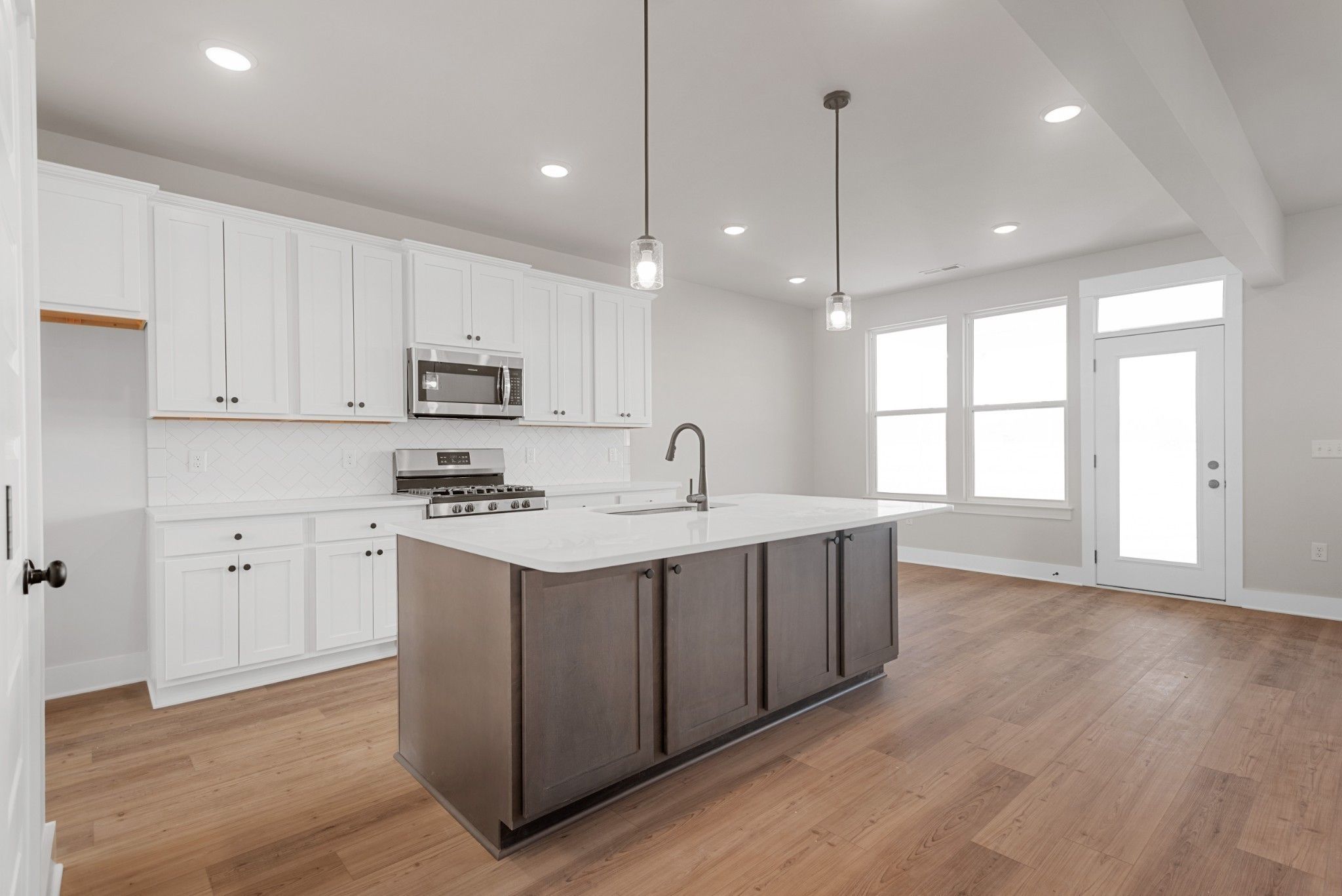 Modern kitchen with white cabinets, large gray island, and stainless appliances in The Willow B plan at Calista Farms.