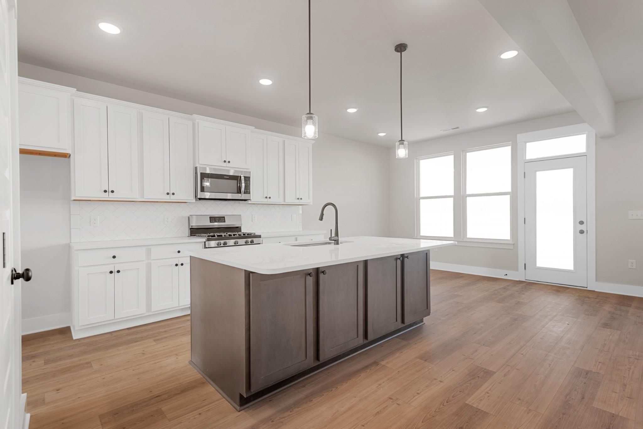 Modern kitchen with white cabinets, large gray island, and stainless appliances in The Willow B plan at Calista Farms.