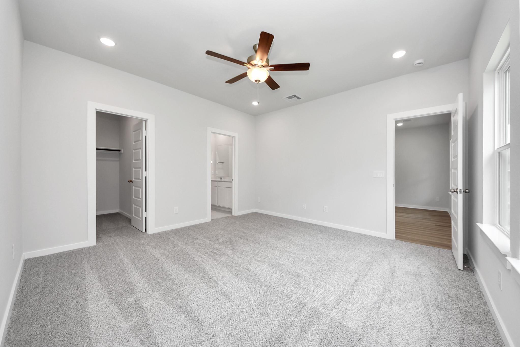 Spacious bedroom with carpet, ceiling fan, and walk-in closet in The Sabine E floor plan at Windmill Estates, Magnolia.