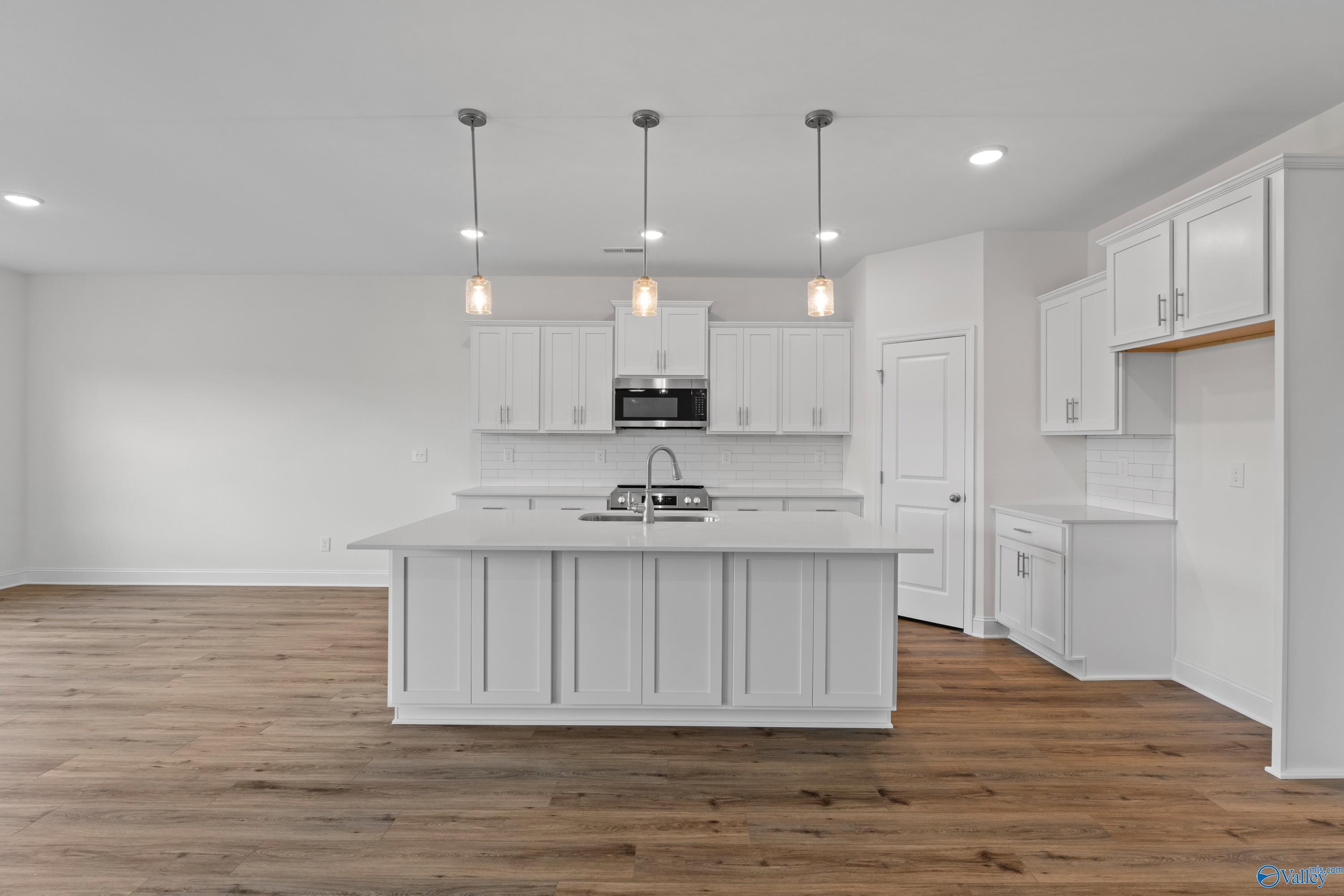 Modern white kitchen island with sink, stainless microwave, pendant lights on hardwood floors in Davidson Homes The Rockford B, Toney, AL