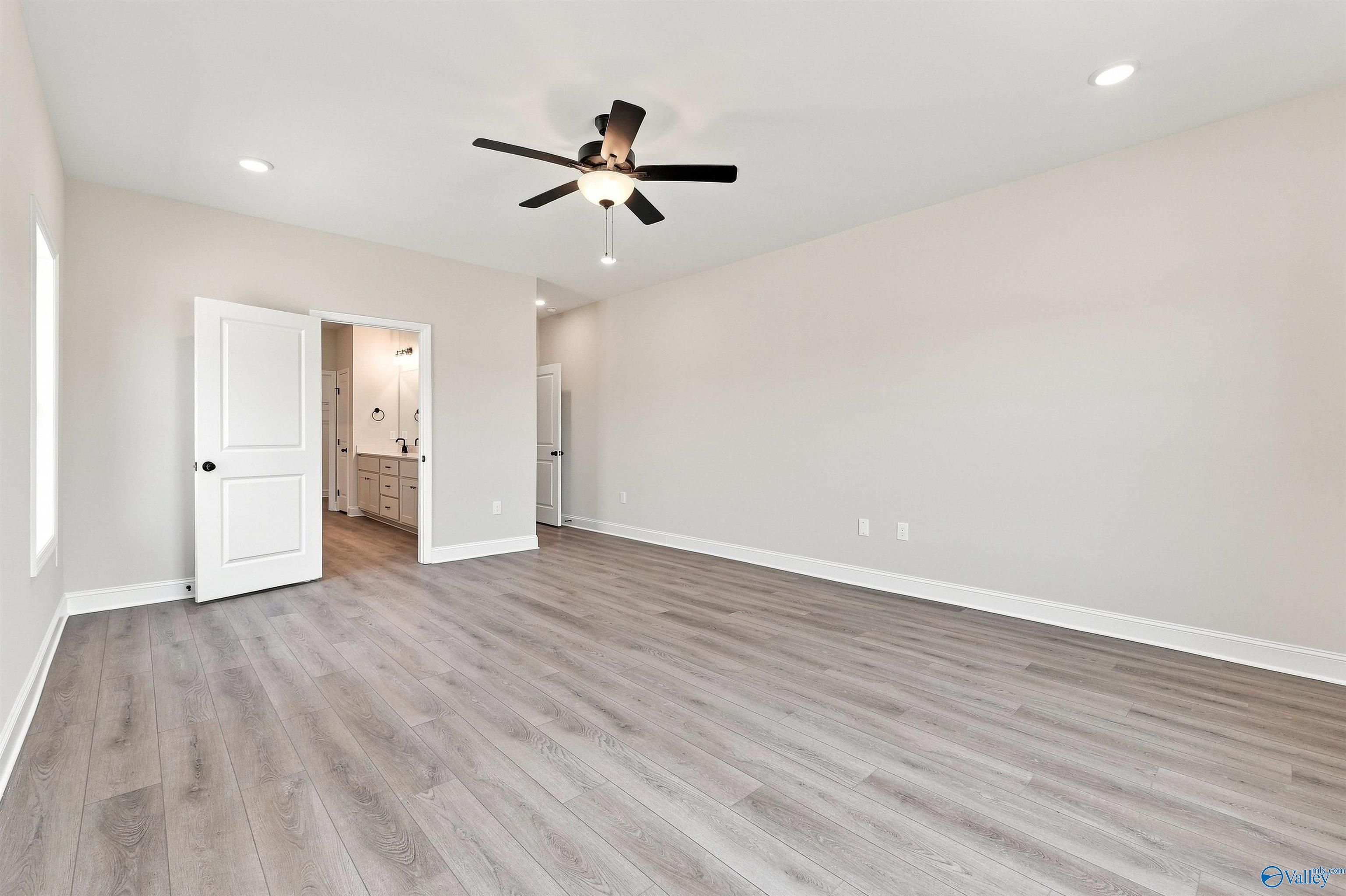 Spacious primary bedroom with modern wood-style flooring and ceiling fan in The Oxford floor plan at Kendall Farms, Toney.